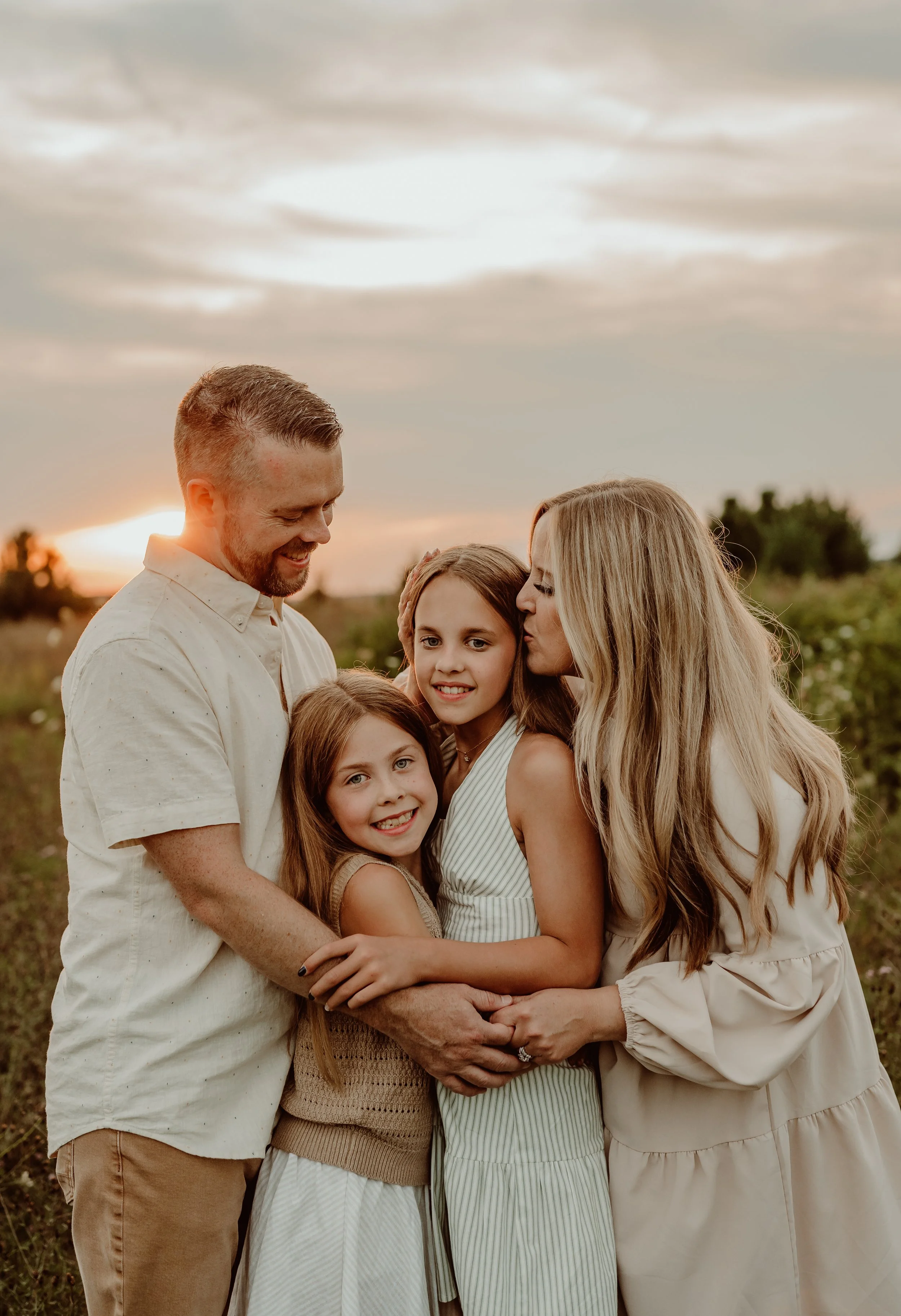 family portrait at golden hour with the family cuddling and the mom giving the daughter a kiss on her head