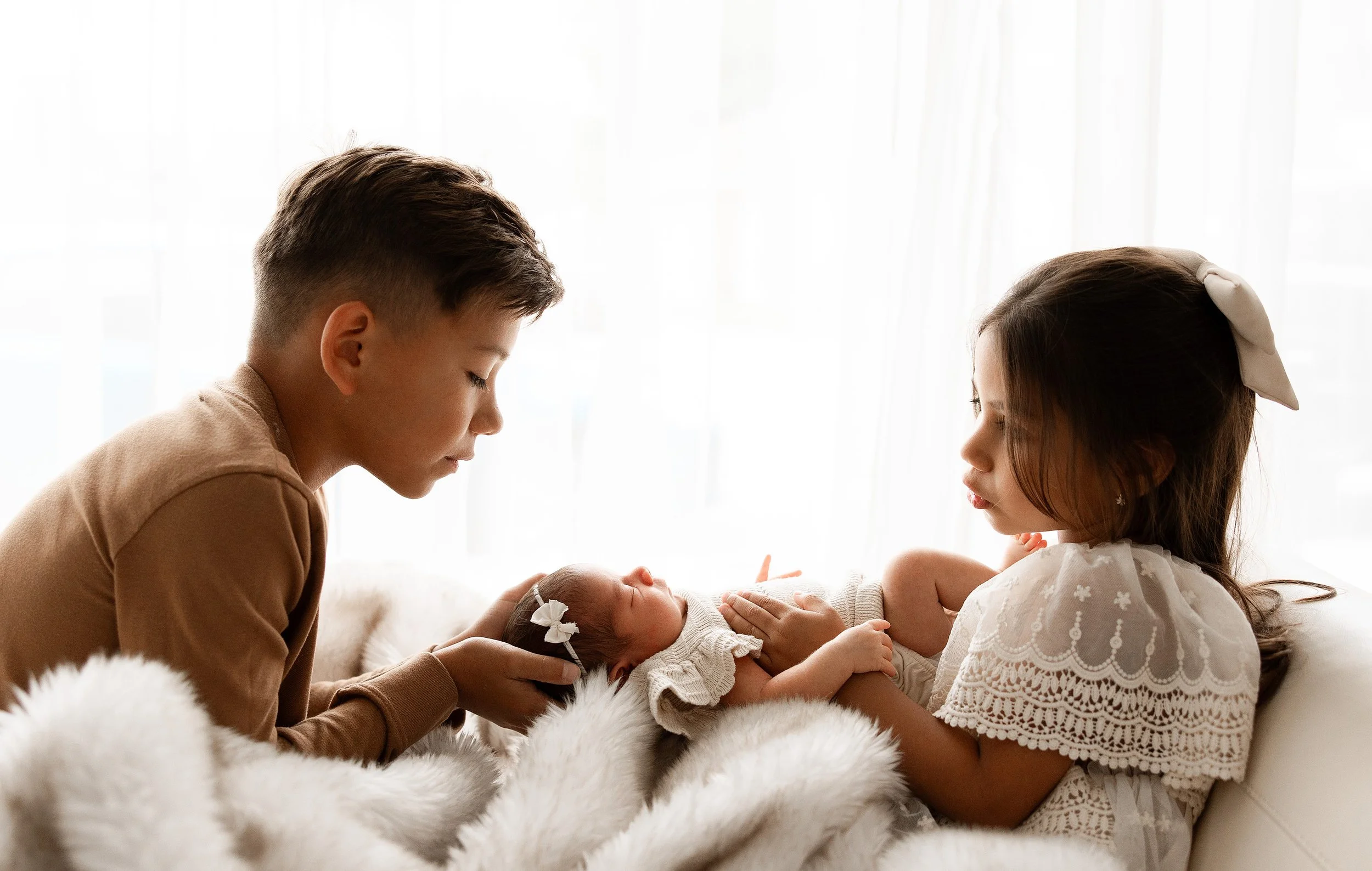 big brother and big sister holding their newborn baby sister in-studio at Chelsie Maurer Photography in Utica, Michigan