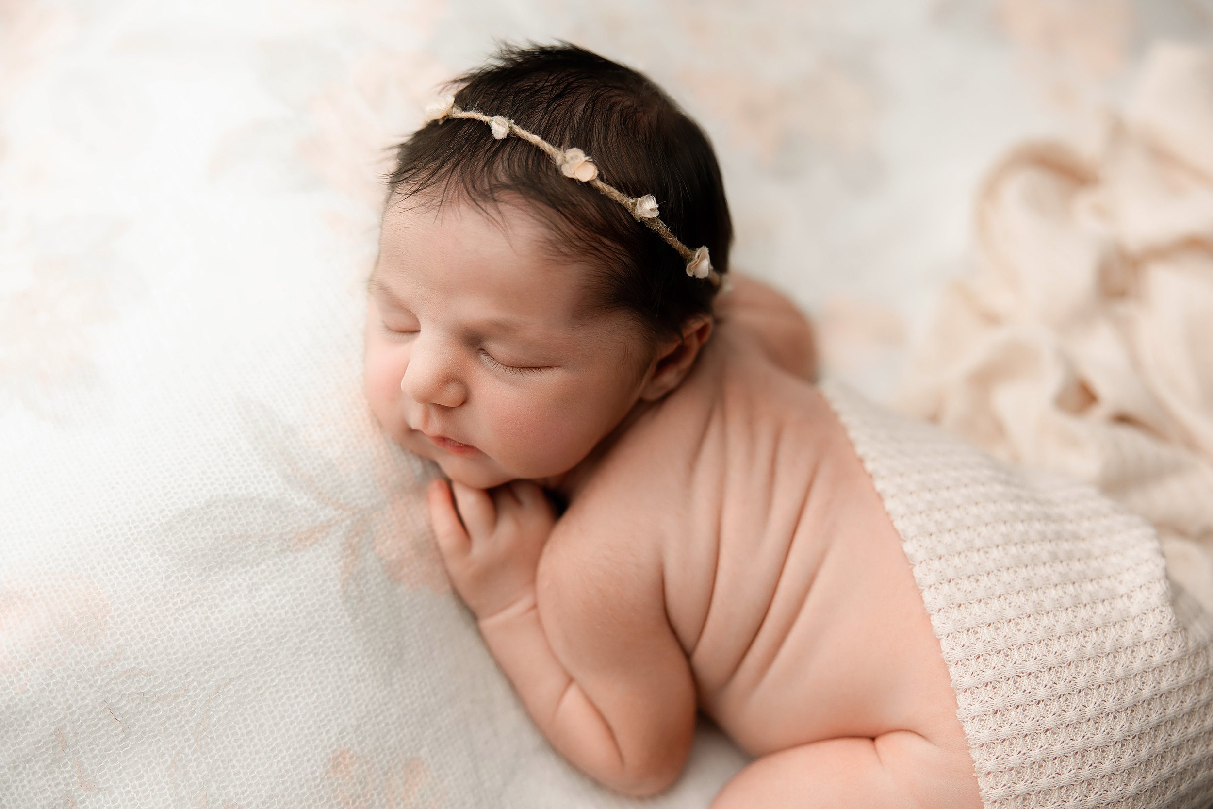 newborn baby girl peacefully sleeping during her photoshoot with a cute dainty headband on and a swaddle gently covering her