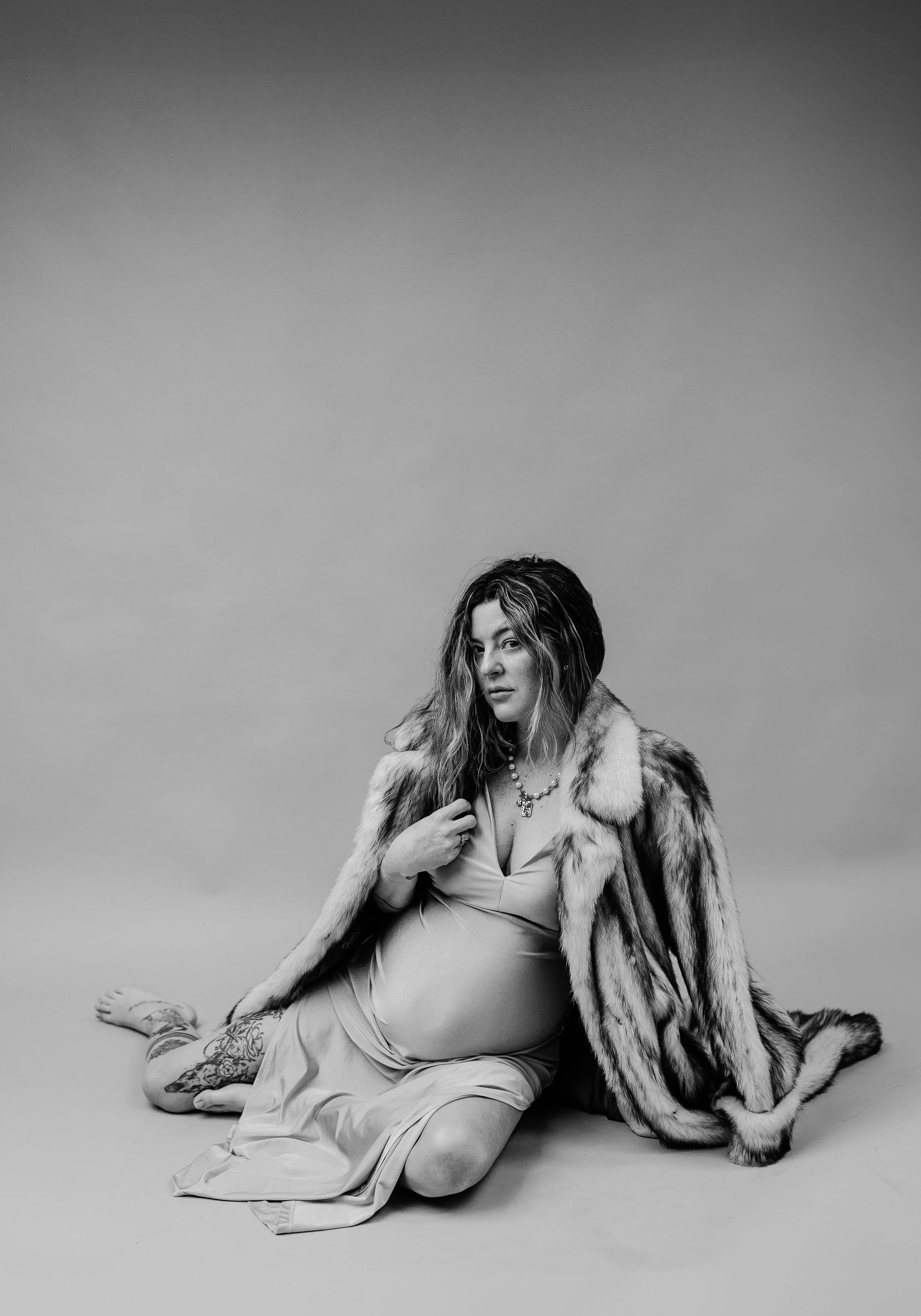 pregnant mother posing for in-studio maternity pictures in a form fitting gold dress and fur coat