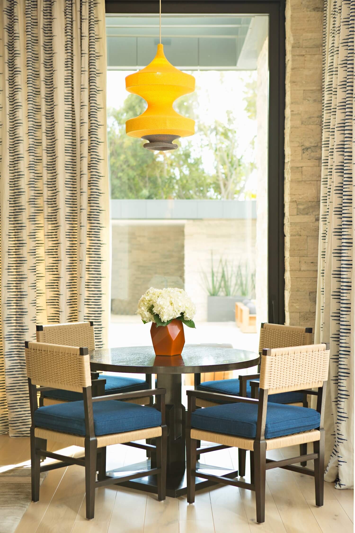 A nook with lacquered table surrounded by cobalt blue upholstered chairs and a Naomi Paul pendant light above.