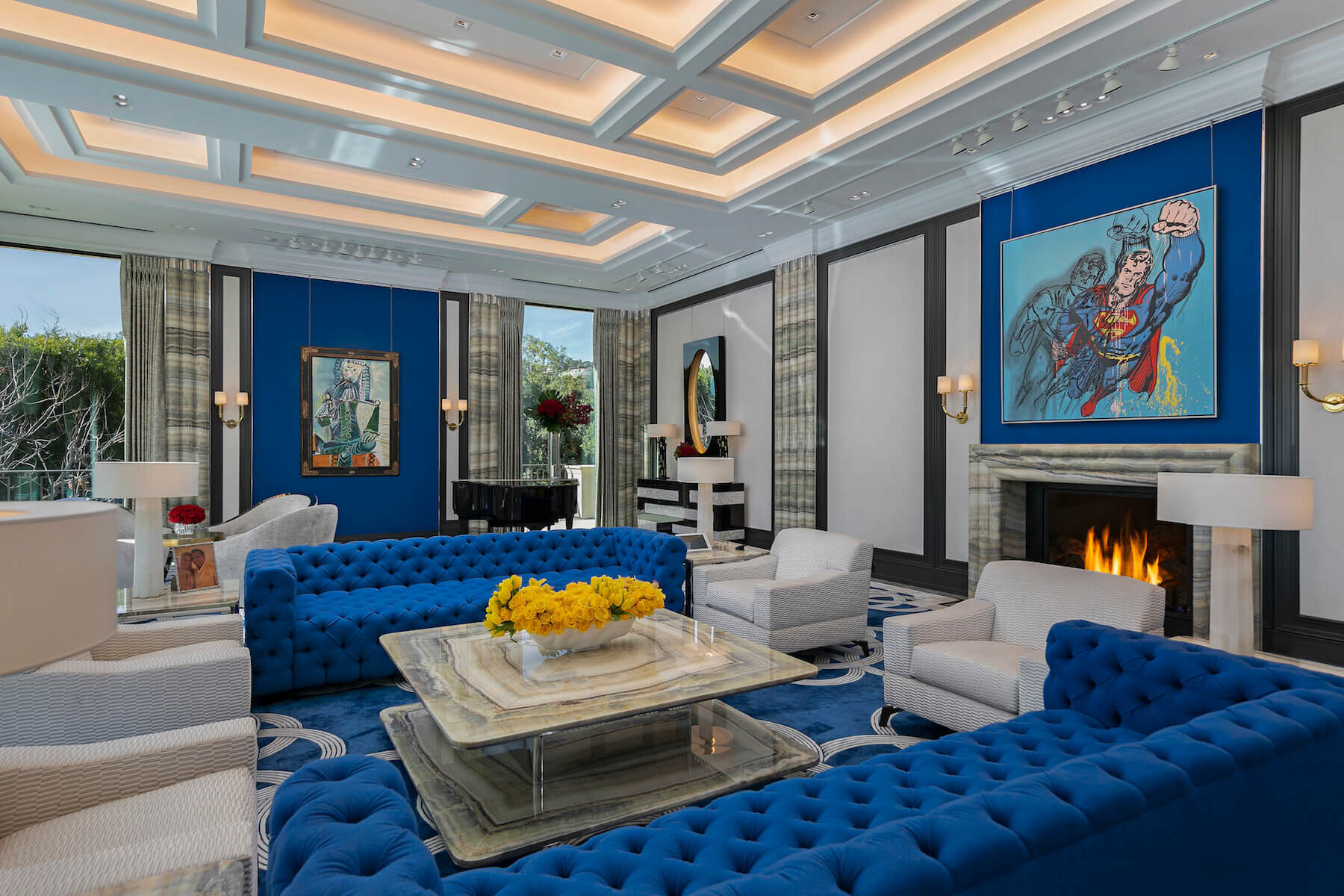 A Great Room filled with coffered ceilings, velvety blue patterned carpet, large floor-to-ceiling windows, and a stately marble fireplace