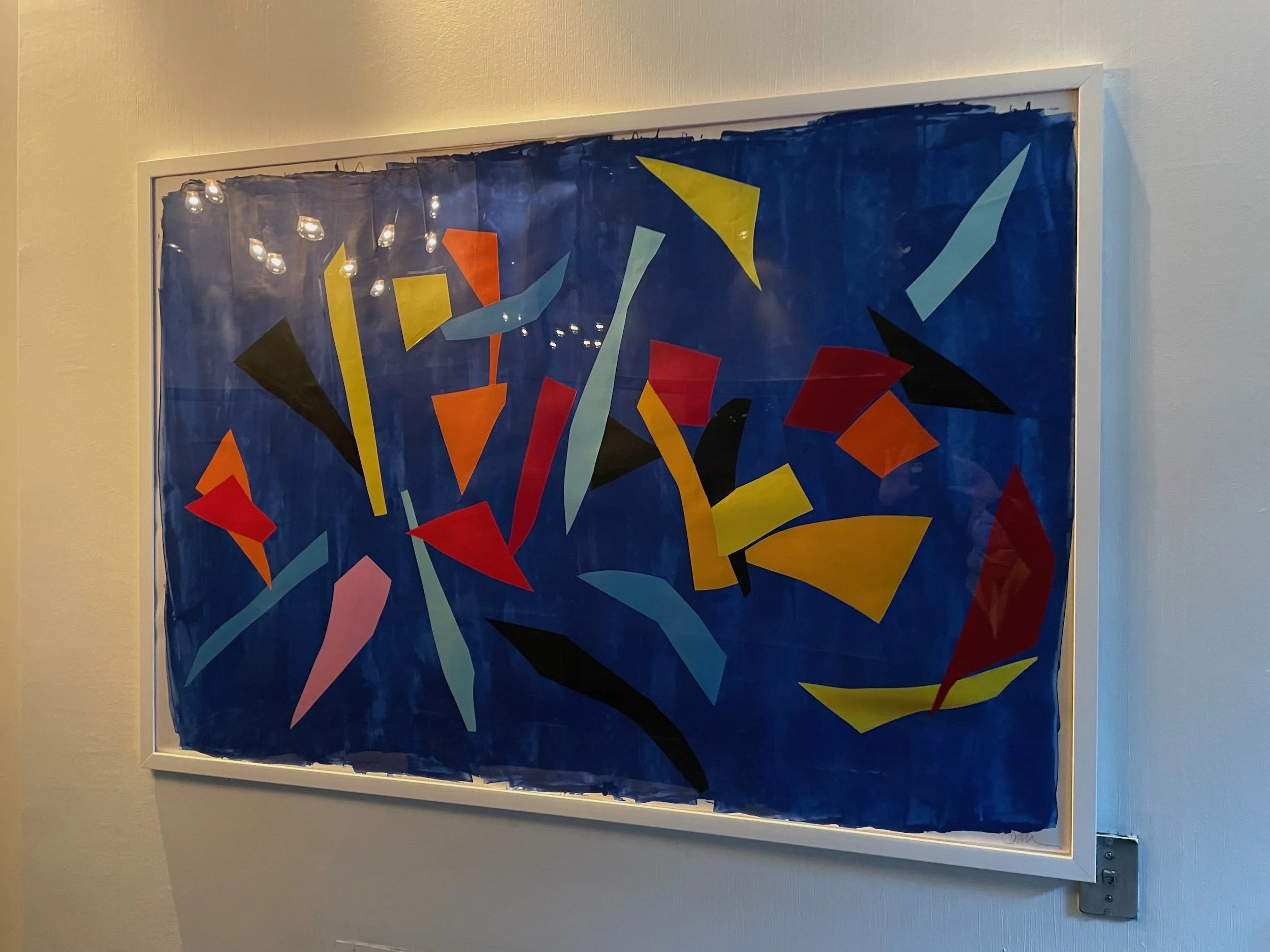 Abstract art with colorful geometric shapes on a blue background displayed in a white frame.