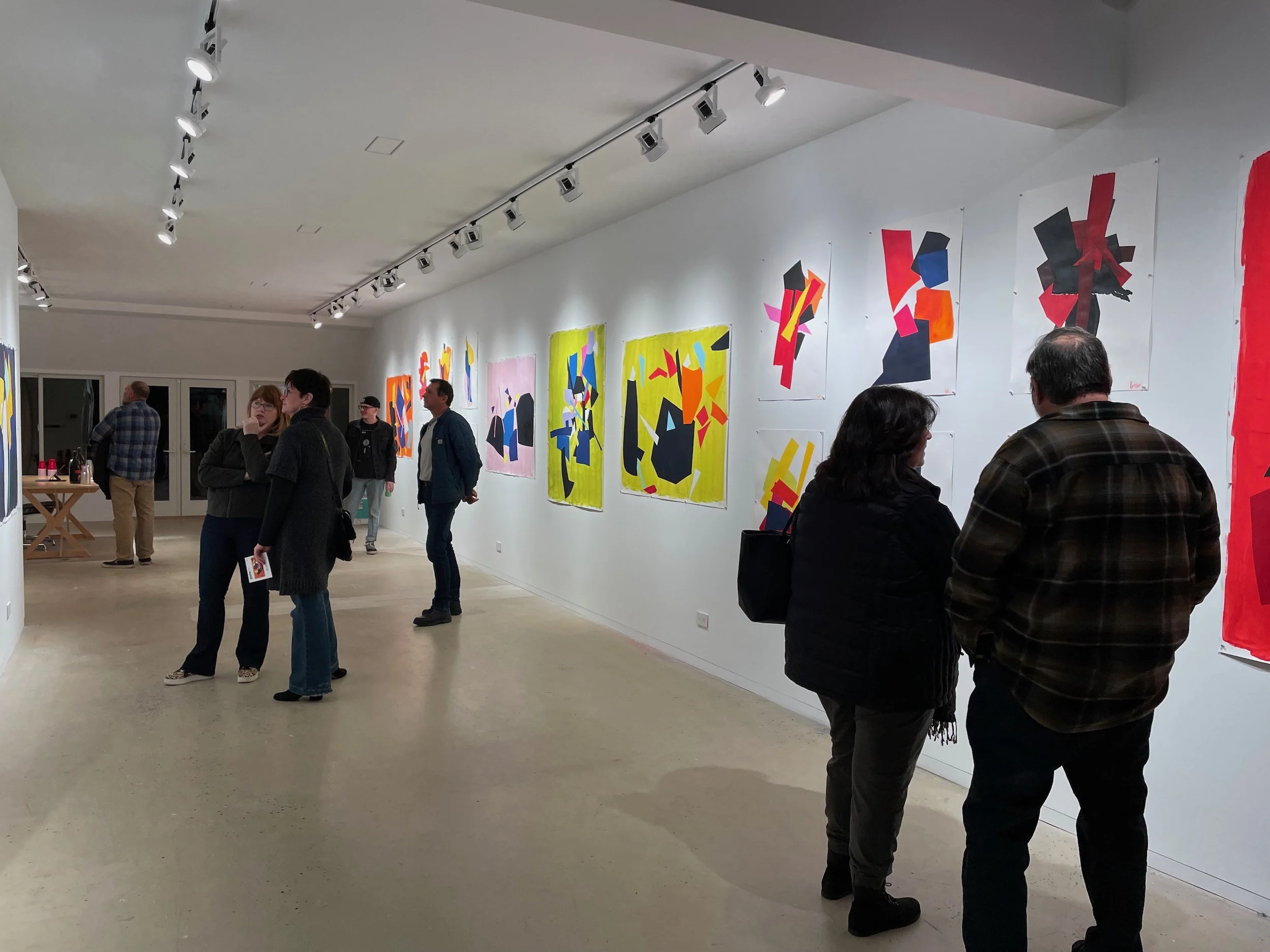 People viewing abstract paintings in an art gallery with white walls and track lighting.