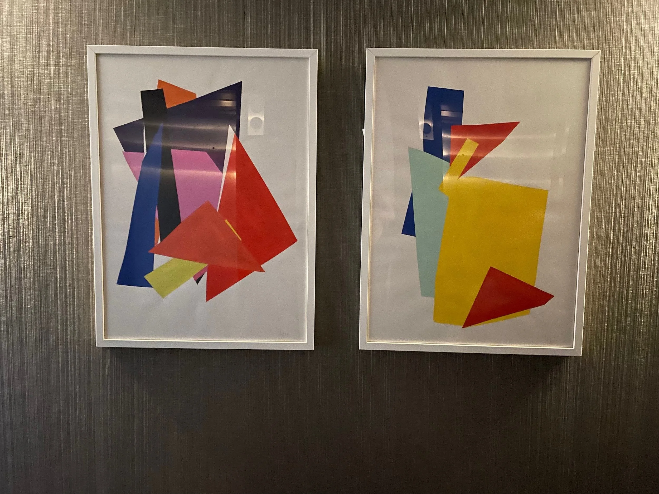Two framed abstract colorful paintings hanging on a textured metallic wall.