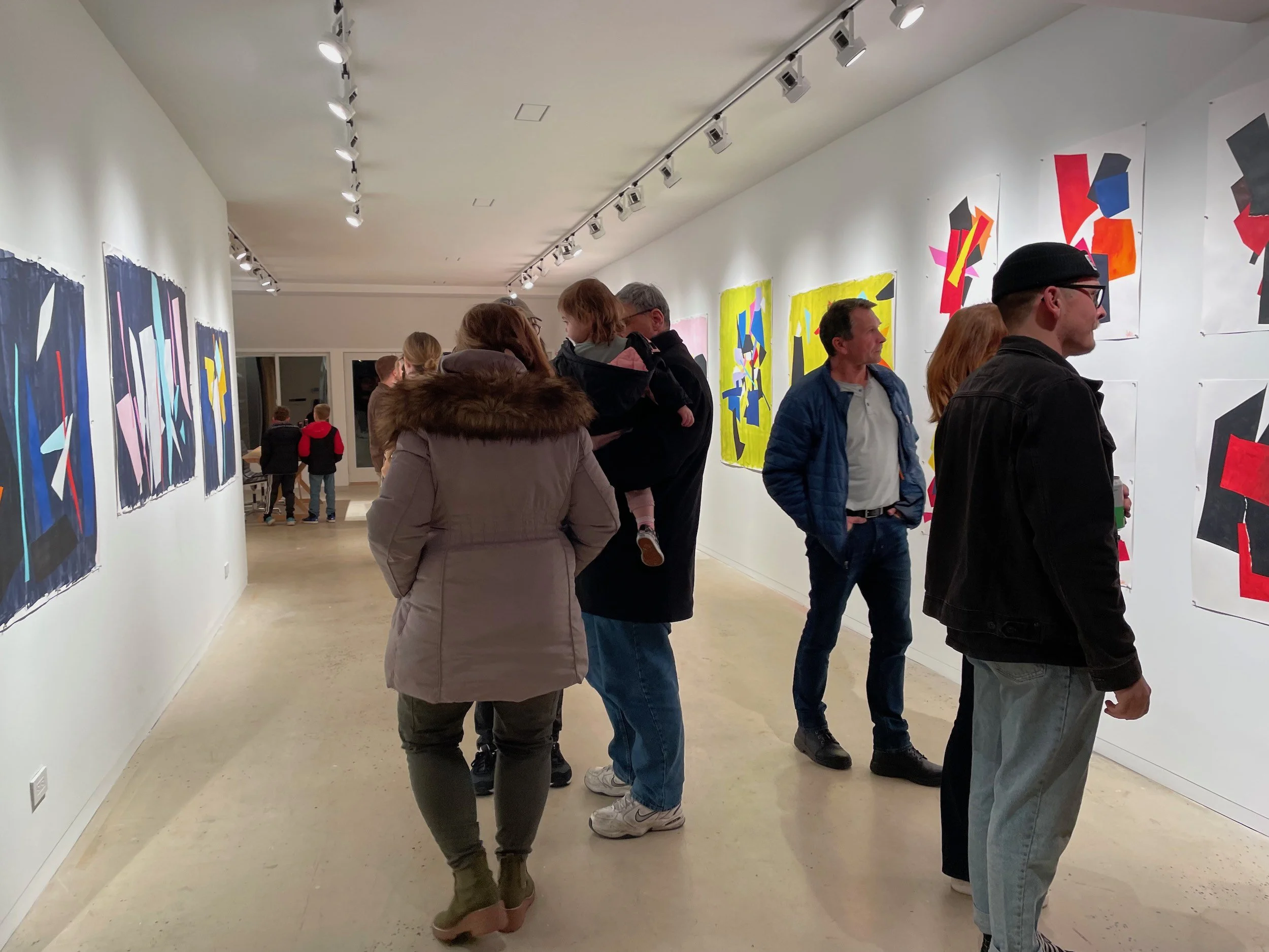 People viewing colorful abstract paintings in an art gallery.