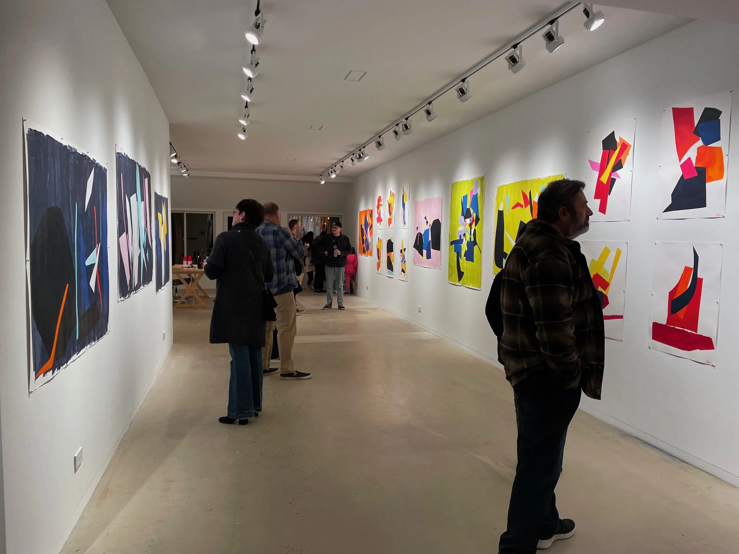 People viewing colorful abstract paintings on gallery walls in an art exhibition.