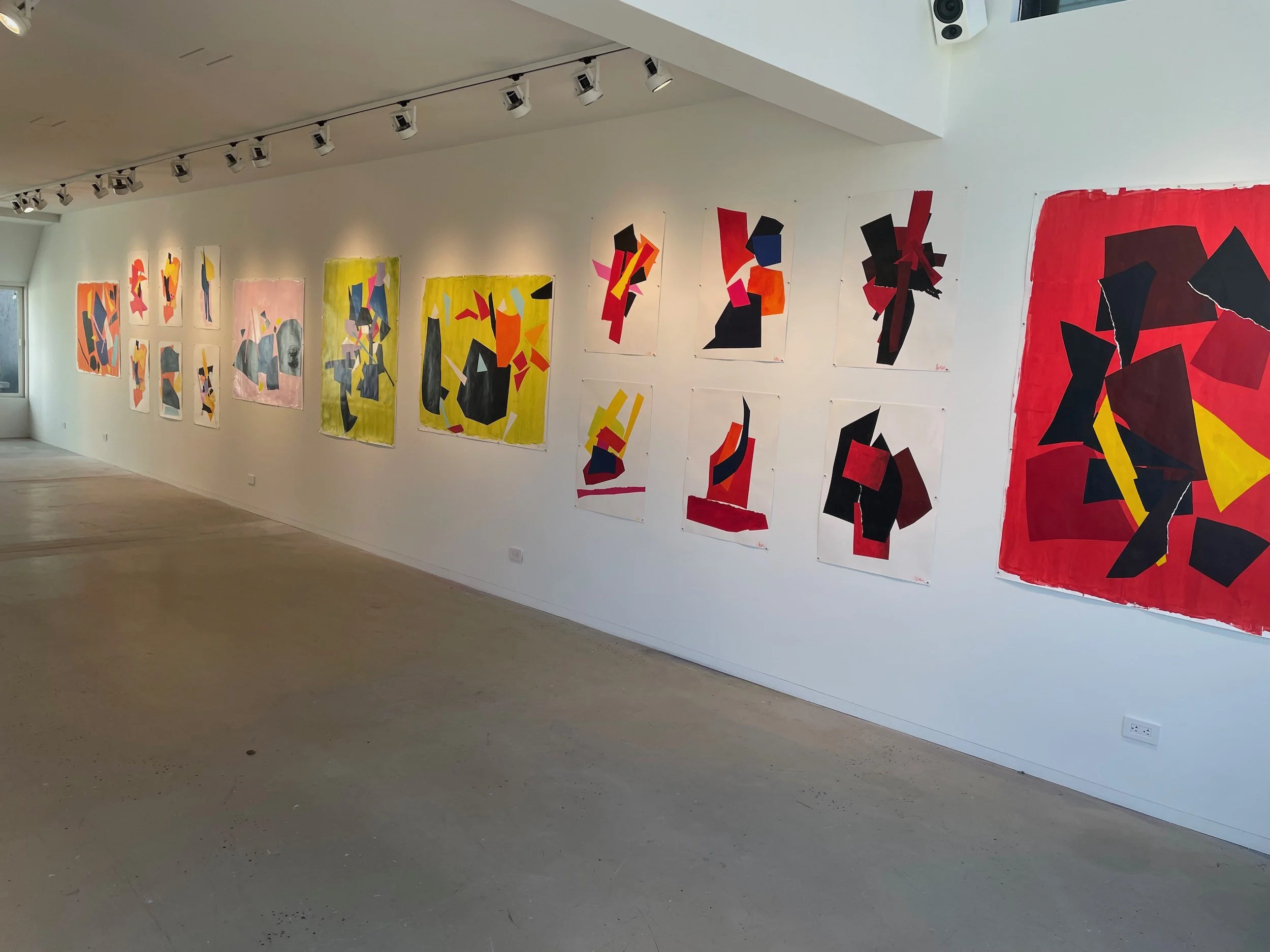 Abstract colorful paintings featuring geometric shapes displayed on a white gallery wall.
