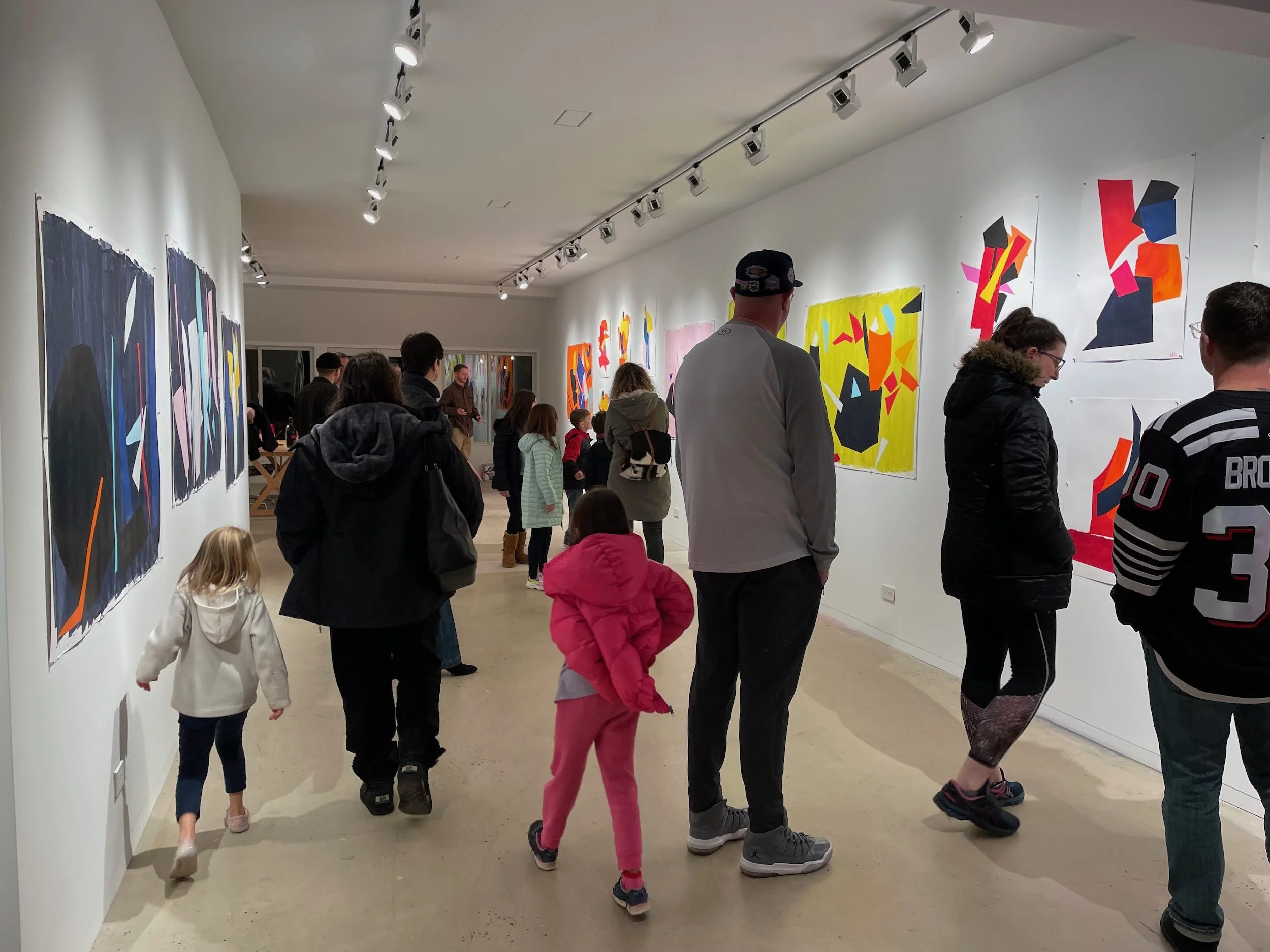 People viewing colorful abstract artwork in an art gallery.