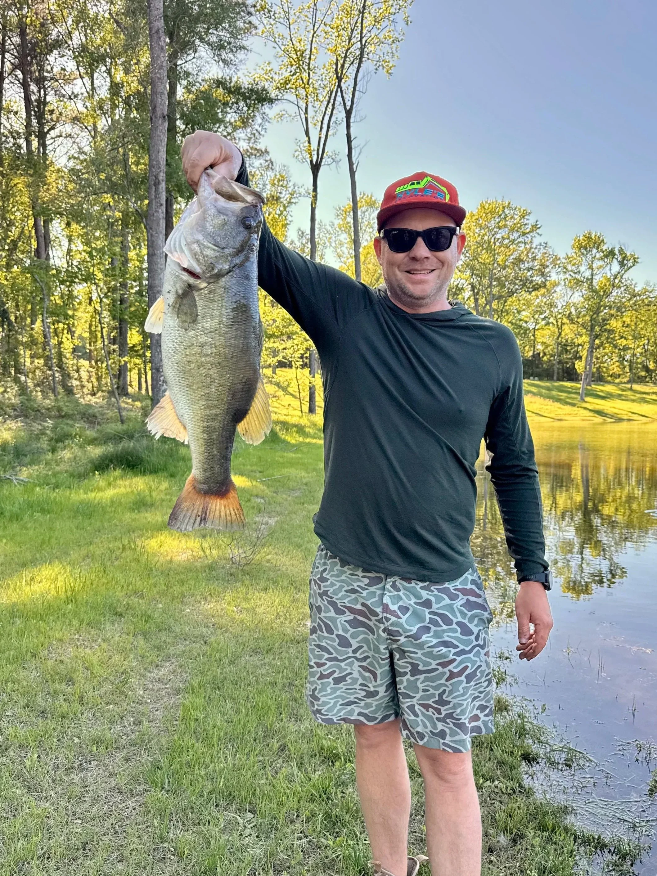 man standing next to lake holding huge largemouth bass