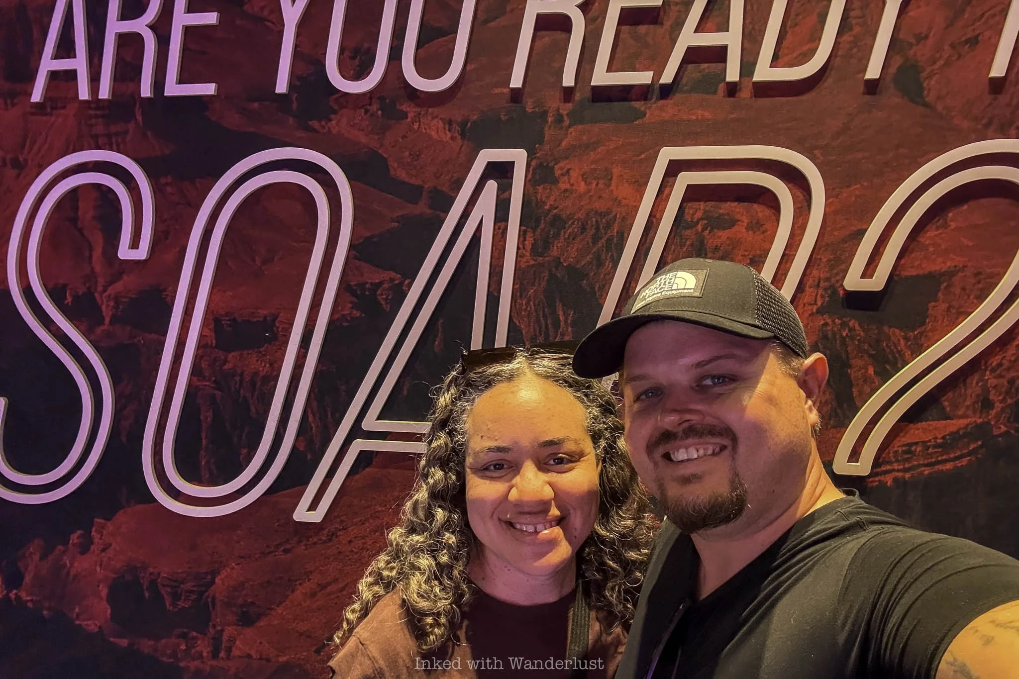 Two people in posing in front of a sign at Flyover Las Vegas.