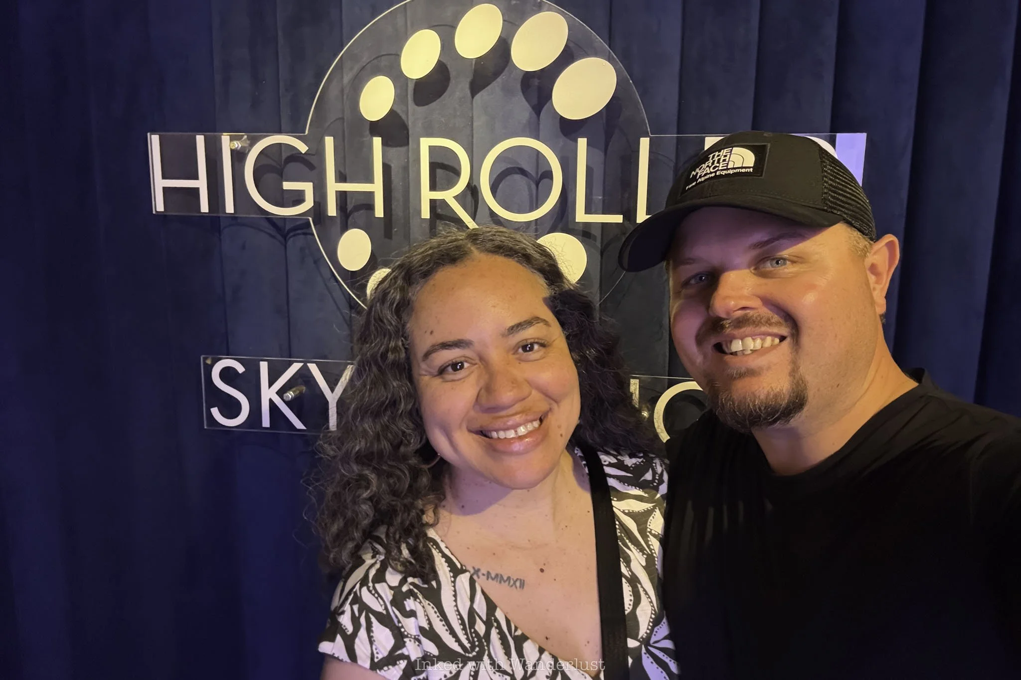 Two people taking a picture with the High Roller Sky Lounge sign.