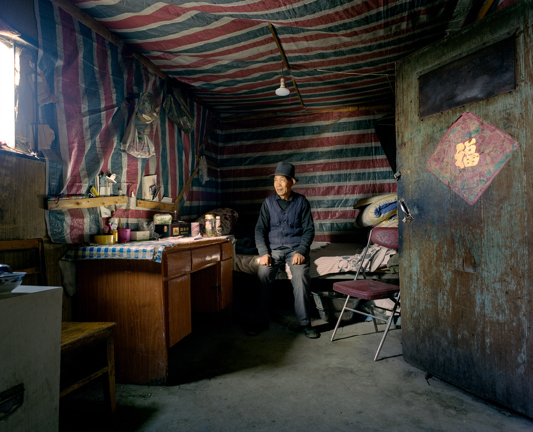  May 2016. Xinjiang province, China. Old Han Chinese man photographed in the bedroom of his house. He is the guardian of a mine in the Taklmakan desert in the western Chinese province of Xinjiang.  