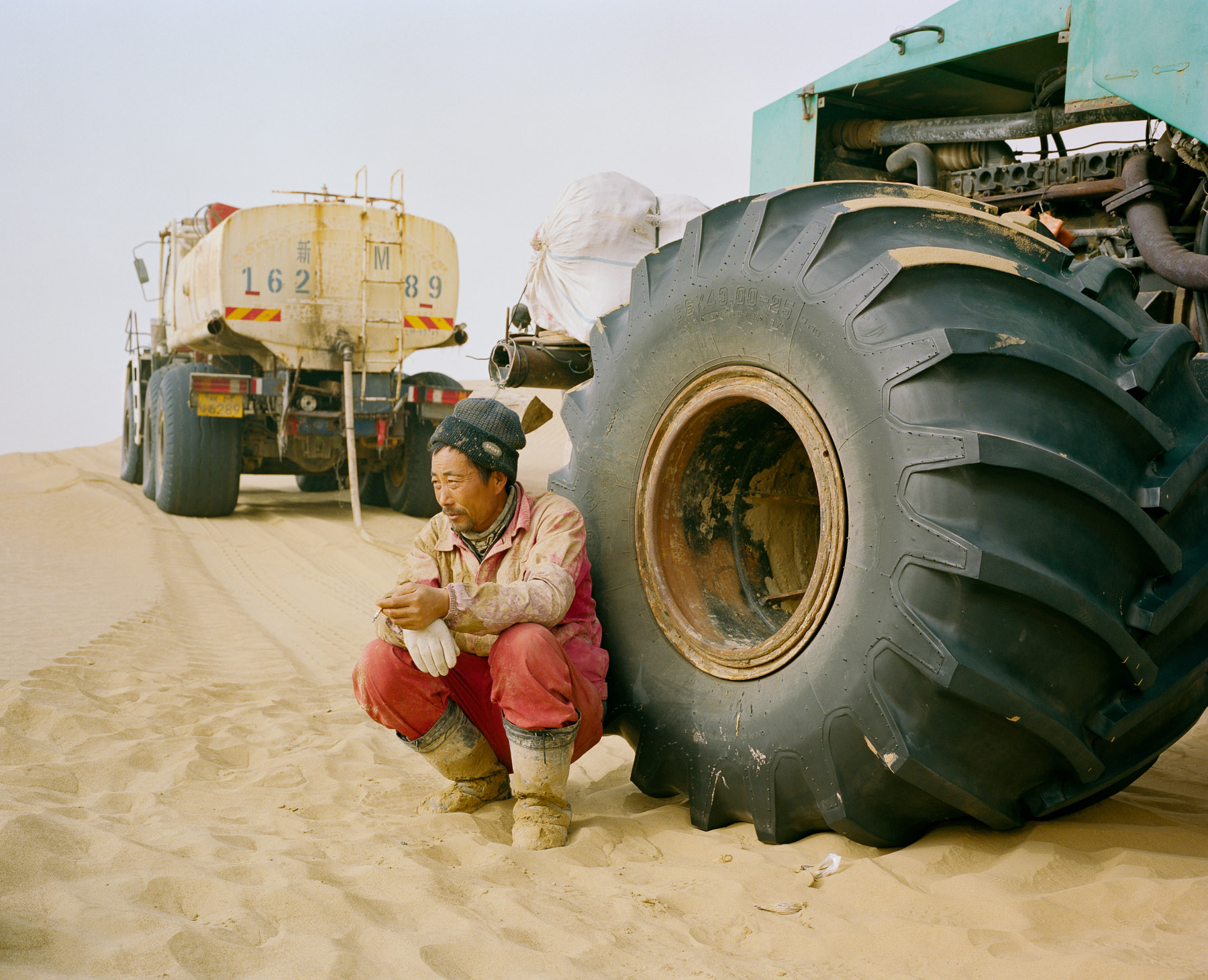  December 2016. Xinjiang province, China. Senior technician from a Chinese state-owned oil company taking a cigarette break after lunch near one of the team's vehicle. He is part of an oil exploration team from a Chinese state-owned company operating