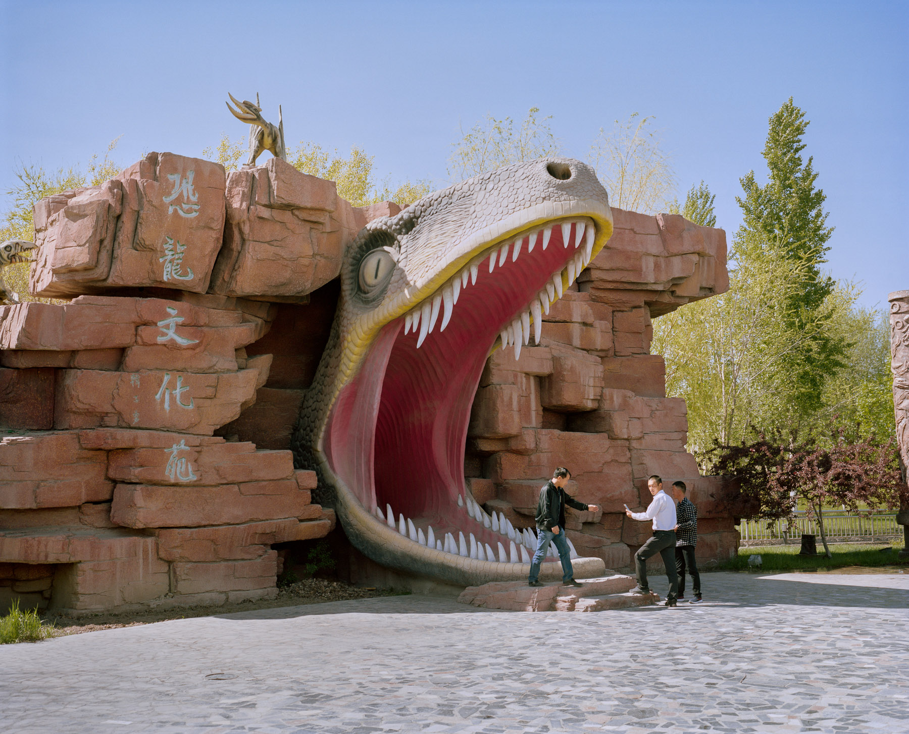  May 2017. Xinjiang province, China. Three Han-Chinese men in the dinosaur-themed amusement park near Wuerhe ghost town in Xinjiang. Fake dinosaur skeleton at the Dinosaur park near Wuerhe Ghost city driving off from Karamai i the North-western part 