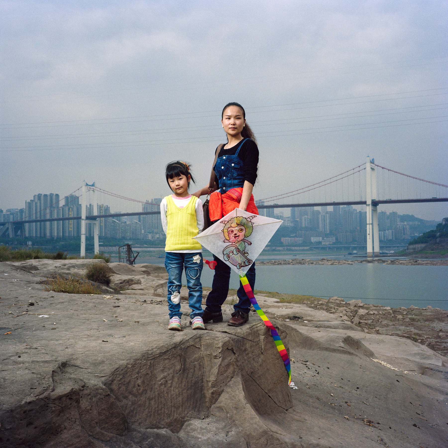  Chongqing, China. 2013. Liu Zhenghui, 33 year-old make-up artist, posing with her daughter on a small rocky island on the Yangtze. In the background the Egongyan bridge （between Nan'an District and Jiulongpo District）鹅公岩大桥  can be seen.
Chongqing is