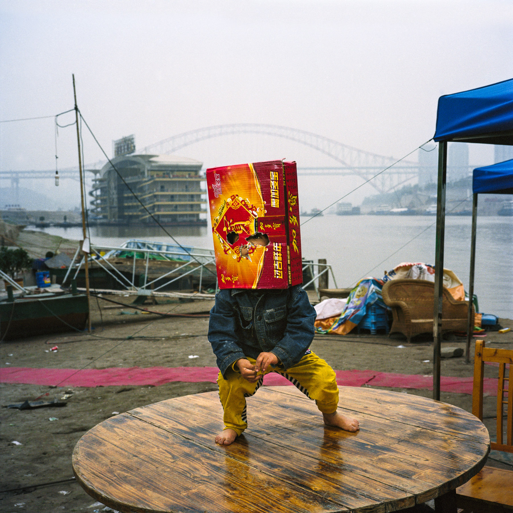  Chongqing, China. 2013. Child with a cardboard bag over his head on the banks of the Yangtze river in downtown Chongqing.
Chongqing is a major city in the Southwest of China and one of the five national central cities in the PRC. It is one of PRC's 
