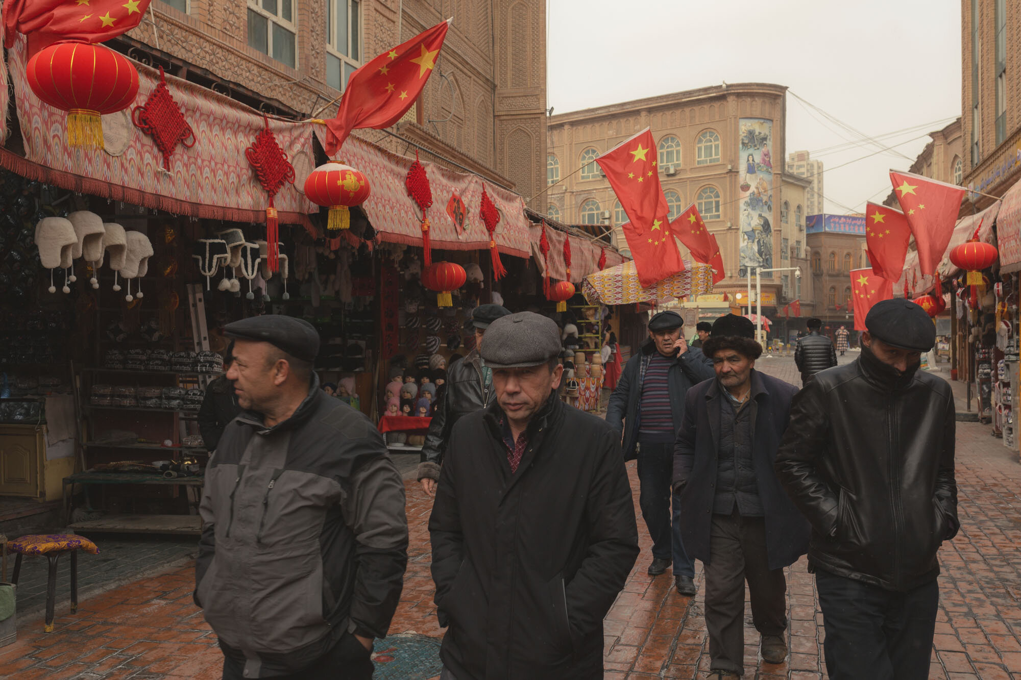  January 31st 2019. Kashgar, Xinjiang province. Uighur-minority men walking in a commercial street full of Chinese flags near the Idkah mosque. 