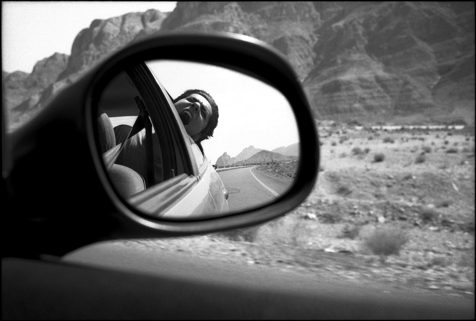  On the road to Yazd, a desert landscape and Mehrad screaming in the rear-view mirror of a Peugeot 206. Yazd, Iran, October 1, 2015. 