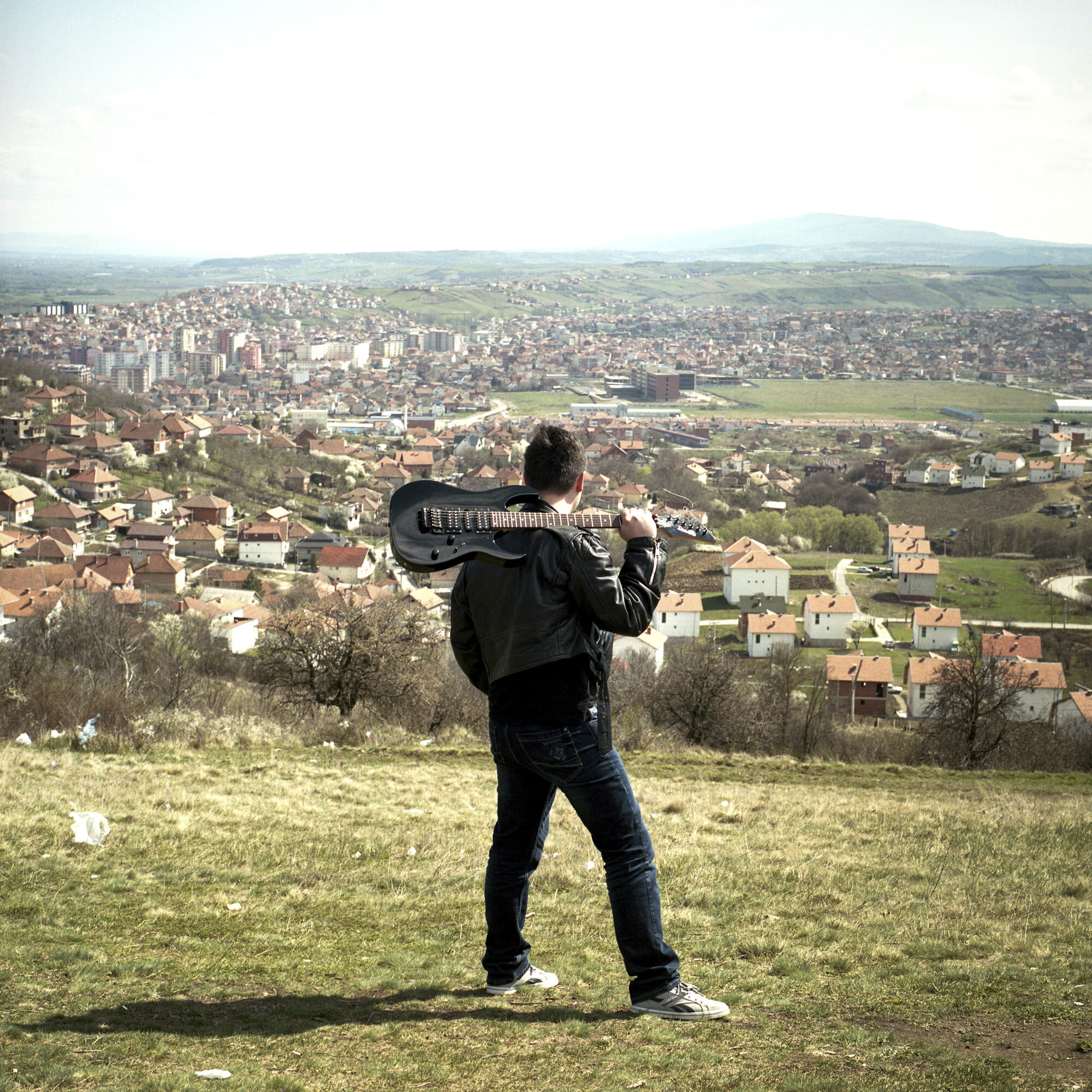 Nemanja Blagojevic, a 23 years old Serb, looks Mitrovica from the heights of the city. He carries his guitar on his shoulder. Mitrovica, Kosovo, March 27, 2017.