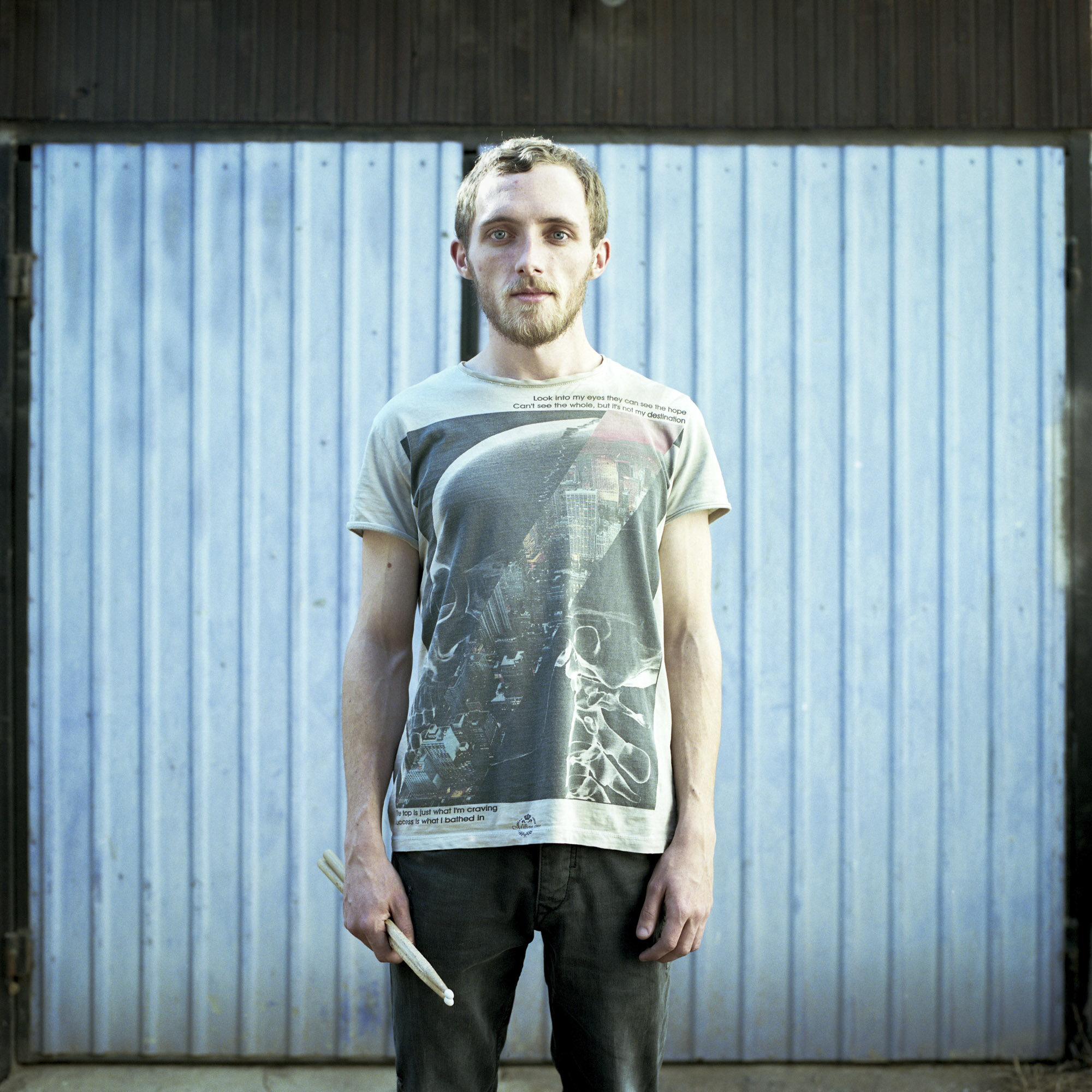 Stefan Kuc holds his drum sticks in front of a blue garage door located in the Serbian side of Mitrovica, Kosovo. Stefan is of Serbian origin. He is student at the Mitrovica Rock School and drummer in the multi-ethnic rock band "Proximity Mine". Mit