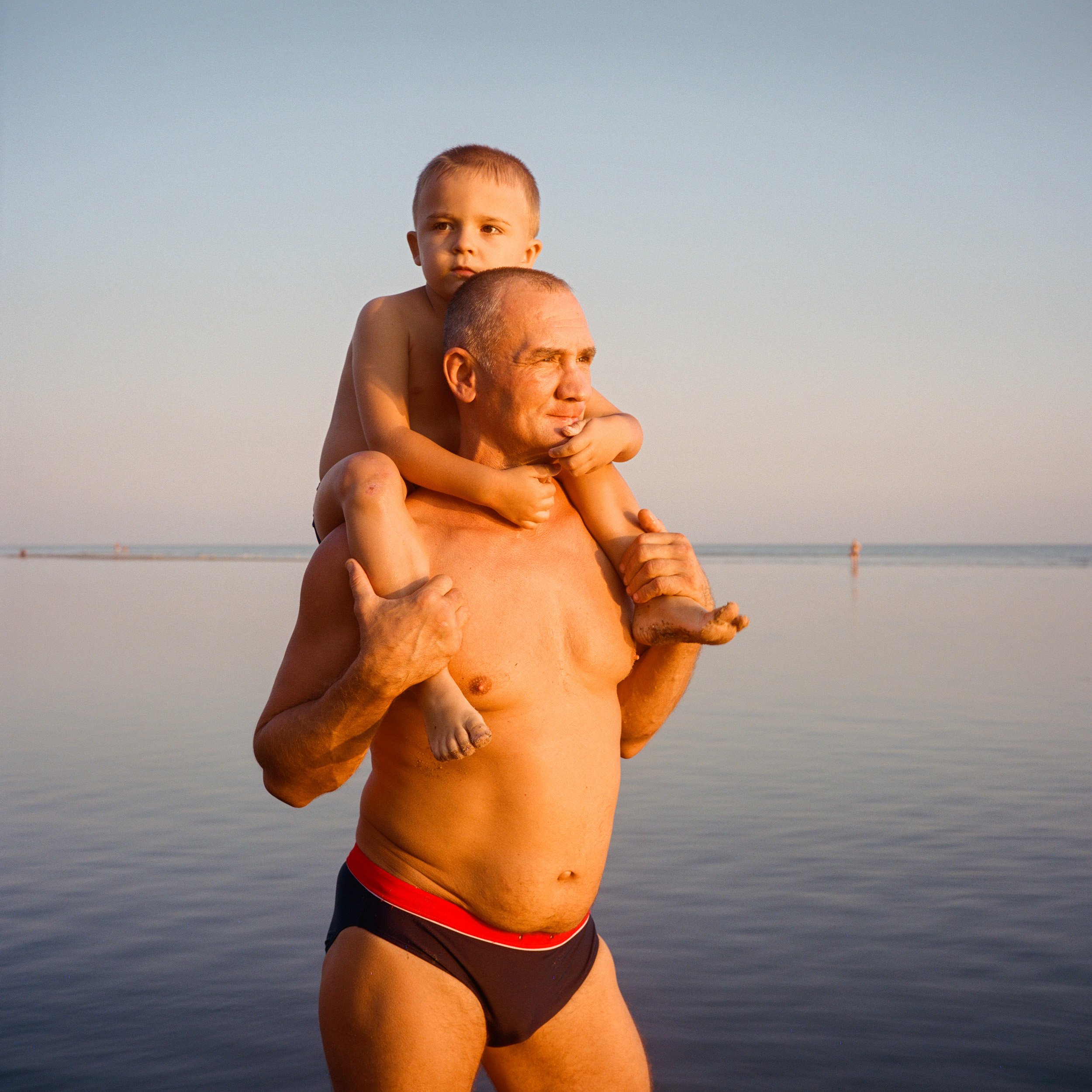  August 2021. Mariupol, Ukraine. Artem Vlasov, 41, and his son Matvey at the beach near the Azovstal steelworks. Artem used to work at the steel plant, the major employer of the industrial city.  