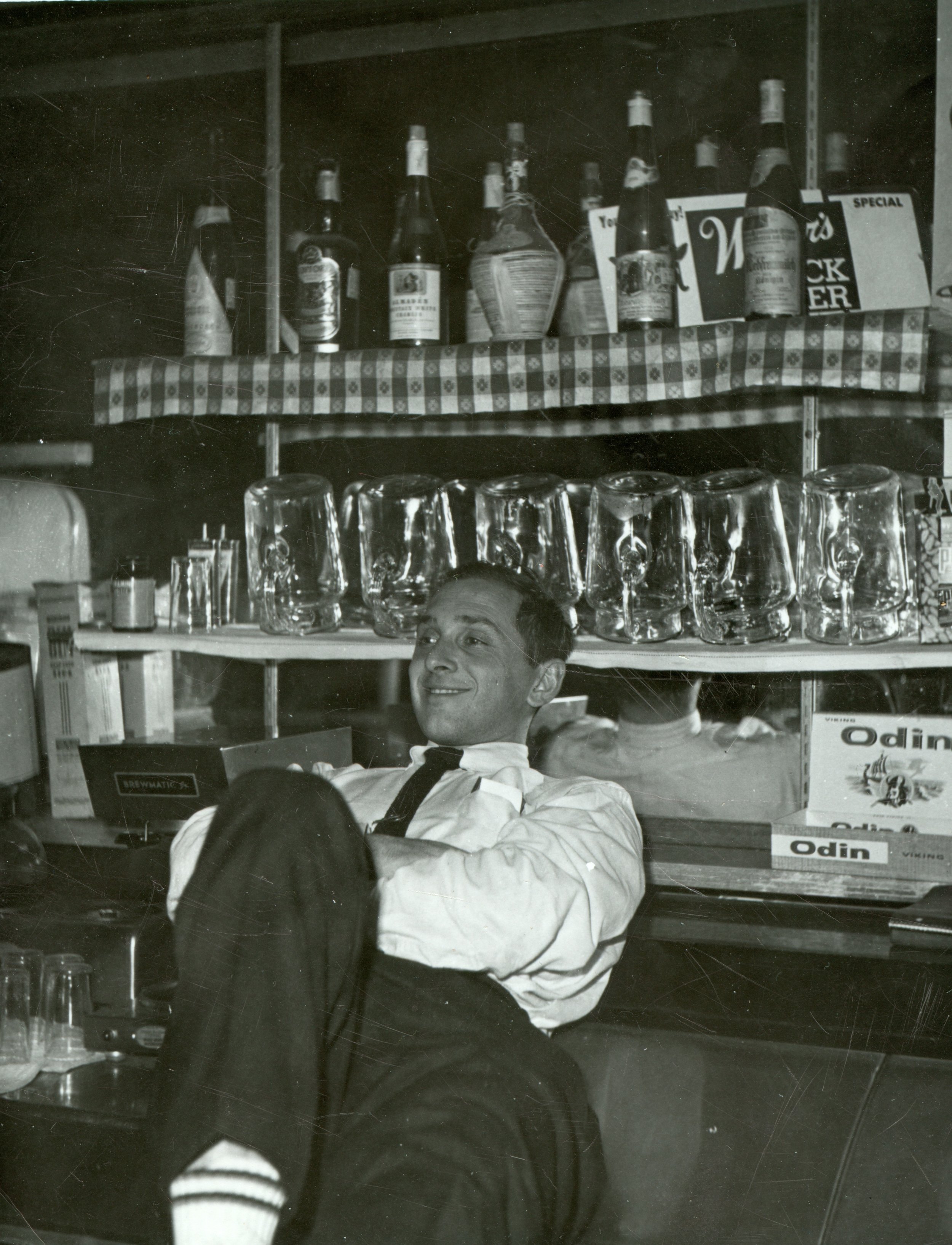 1950s owner , Floyd Marks, sits with his back against the bar, black and white image