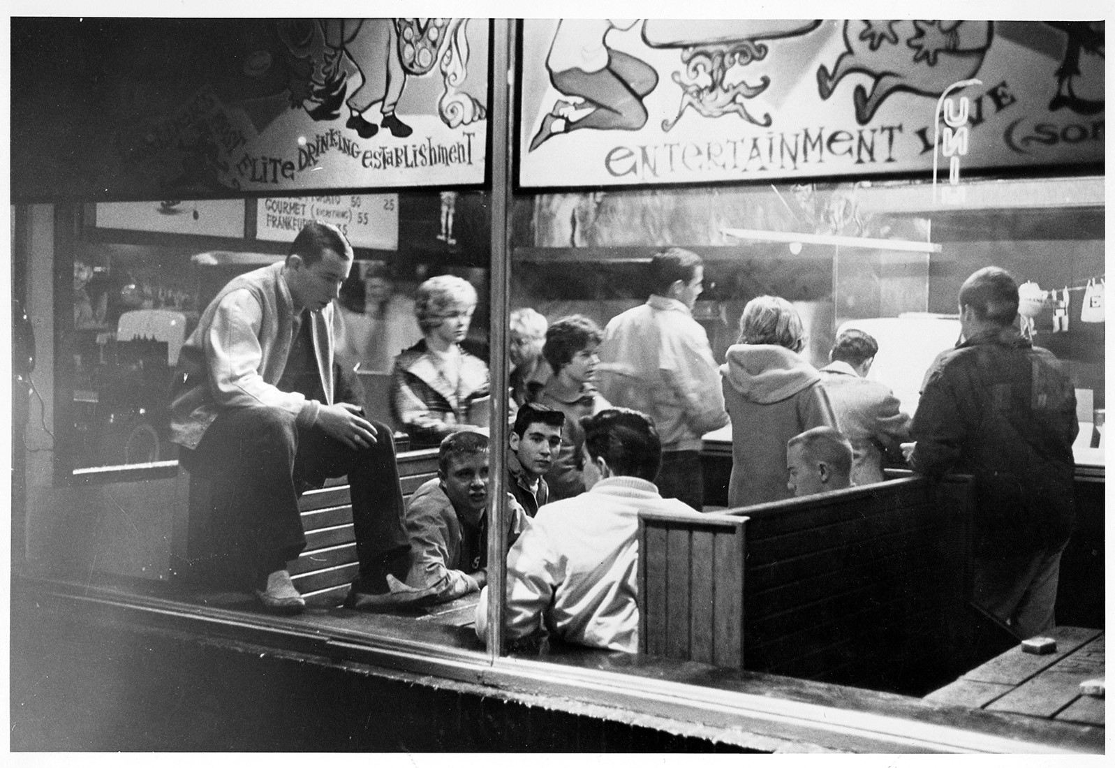 A look through the window into the entrance of The Sink circa 1950s. Guests sitting in wooden booths enjoying the best burgers in Boulder