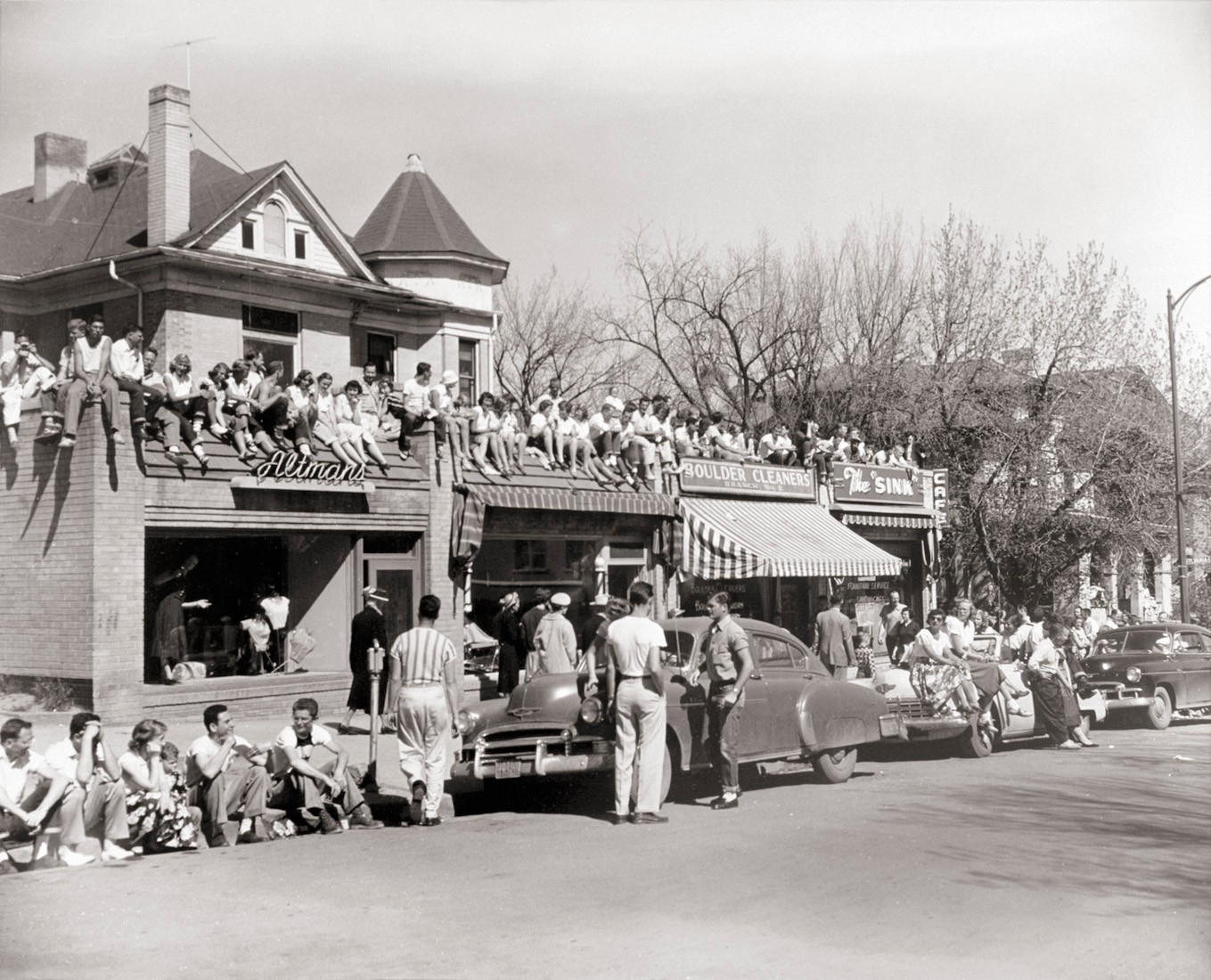 Black and white photo from the 1950s. Lines of collage aged students and locals lining 13th street on the hill. People are on the streets and on the roofs of The Sink and neighboring stores.