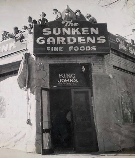 Homecoming in the 1940s. People are on the roof of The Sink. Sign says The Sunken Gardens Fine Foods and underneath it says King Johns on the door 