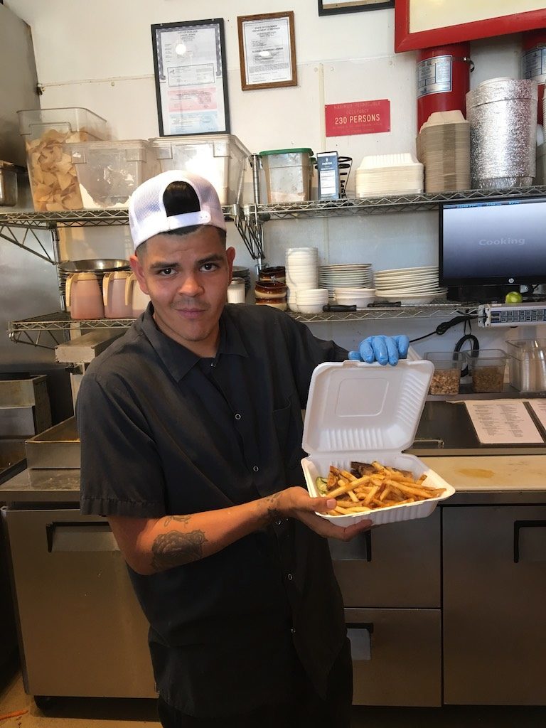 Sink kitchen employee holding a compostable take out container of food