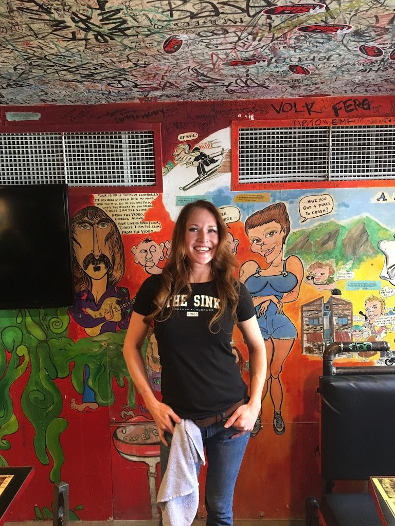 Sink waitress posing in front of an iconic sink wall with art and signatures on the ceiling