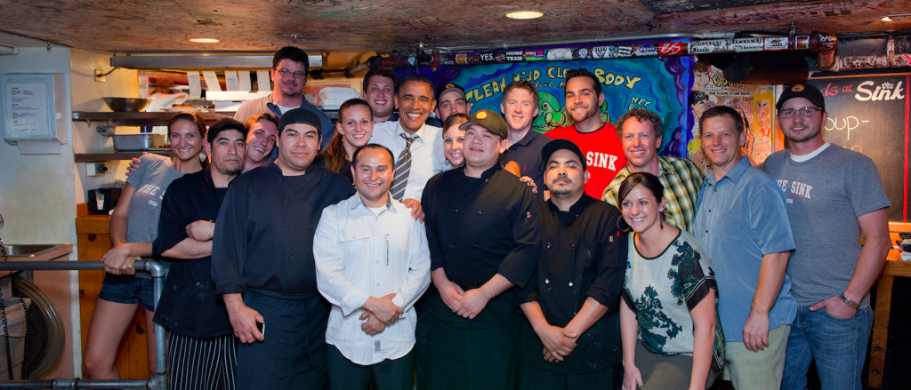 Group shot of Sink employees and owners surrounding President Barak Obama in front of the expo window