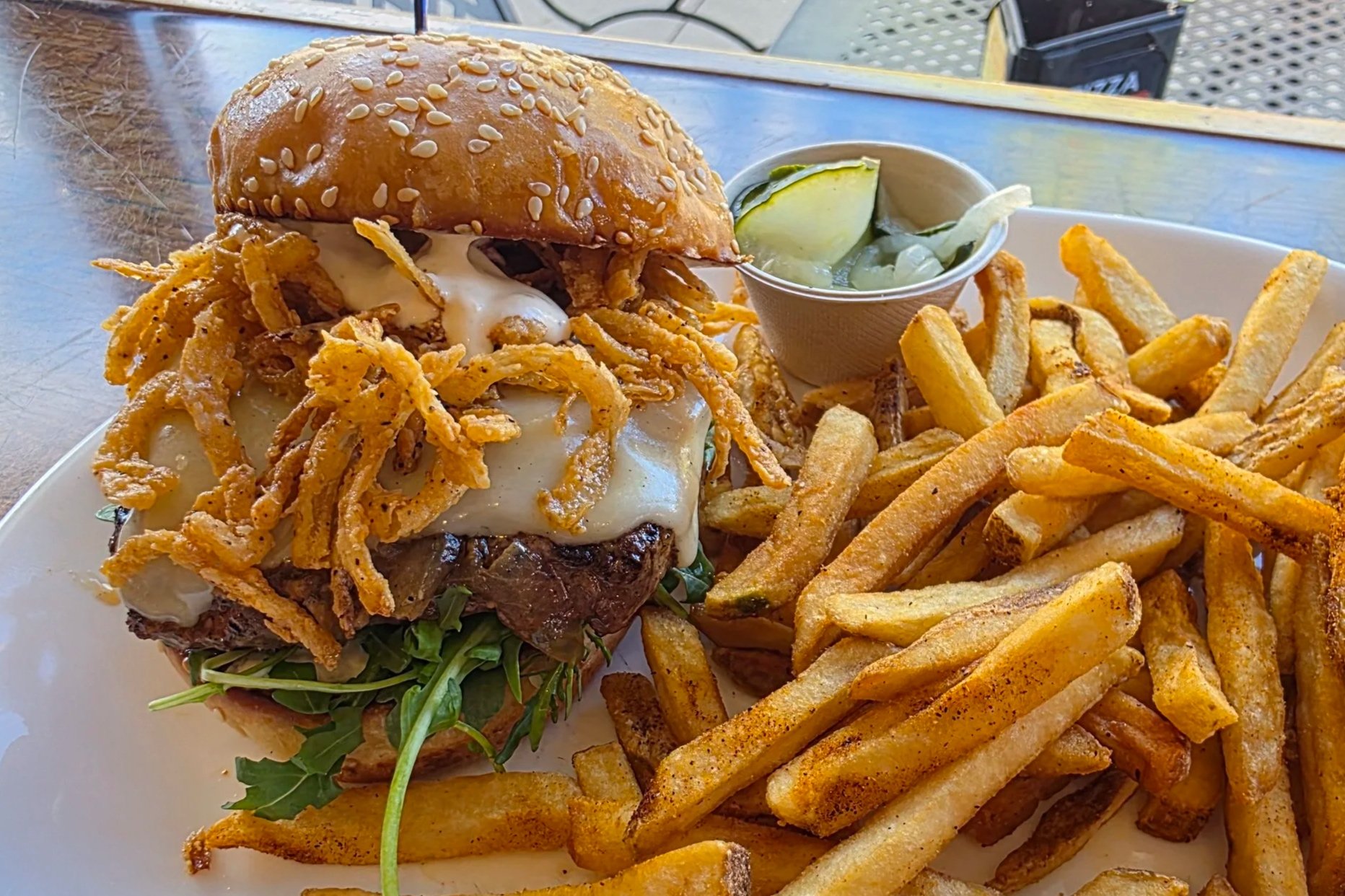 A Grass-fed Colorado beef patty topped with tender, slow-cooked onions, Swiss cheese melted with a splash of rich beef broth, crispy onion straws, and horseradish sauce and a side of house-made pickles
