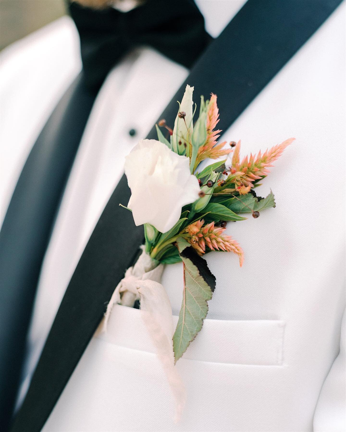 White tux, black lapels, and an ocean- coral inspired boutonniere.