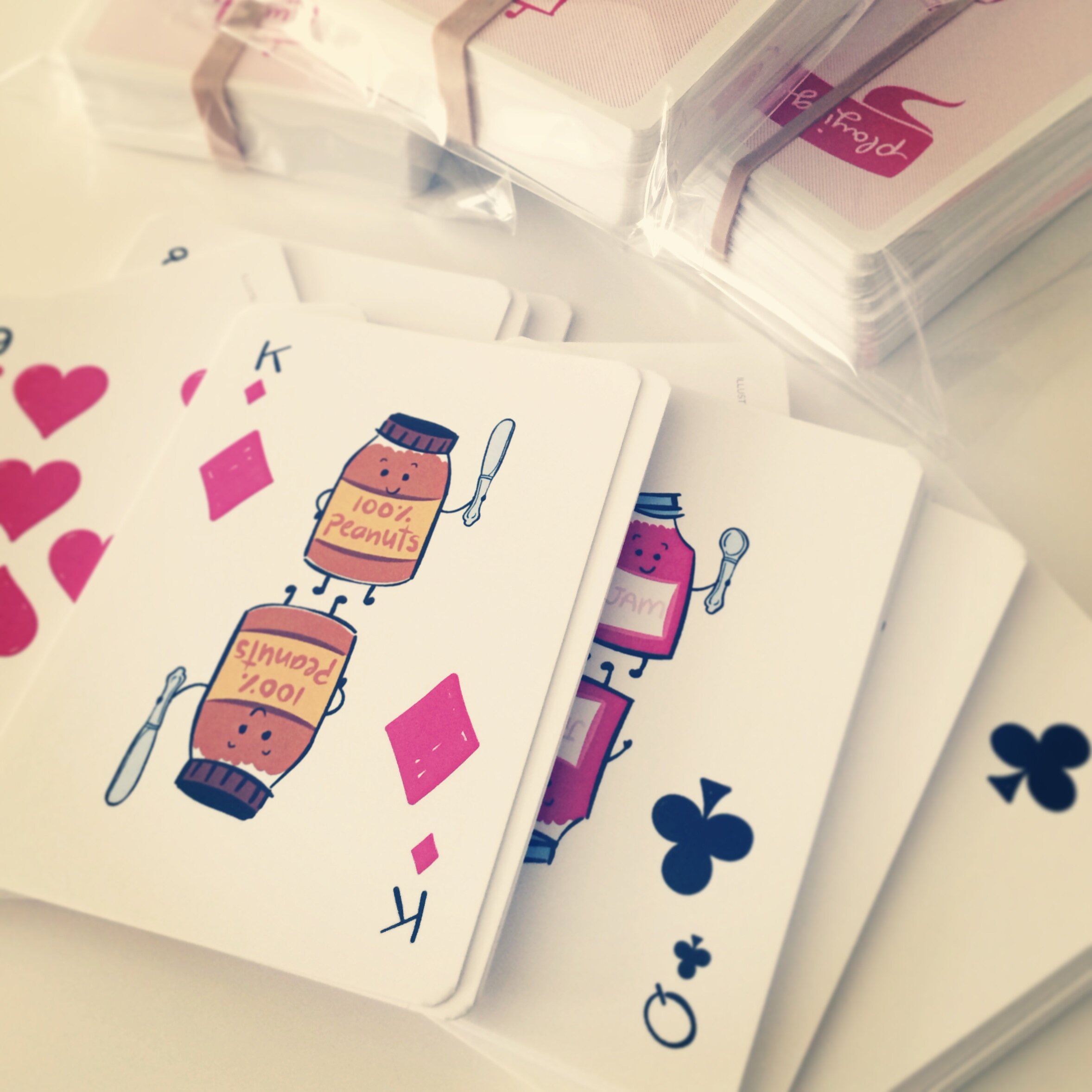  Photo of a deck of playing cards spread out on a table. The card on top is the King of Diamonds, depicting a mirrored illustration of a jar of peanut butter holding a butter knife. 