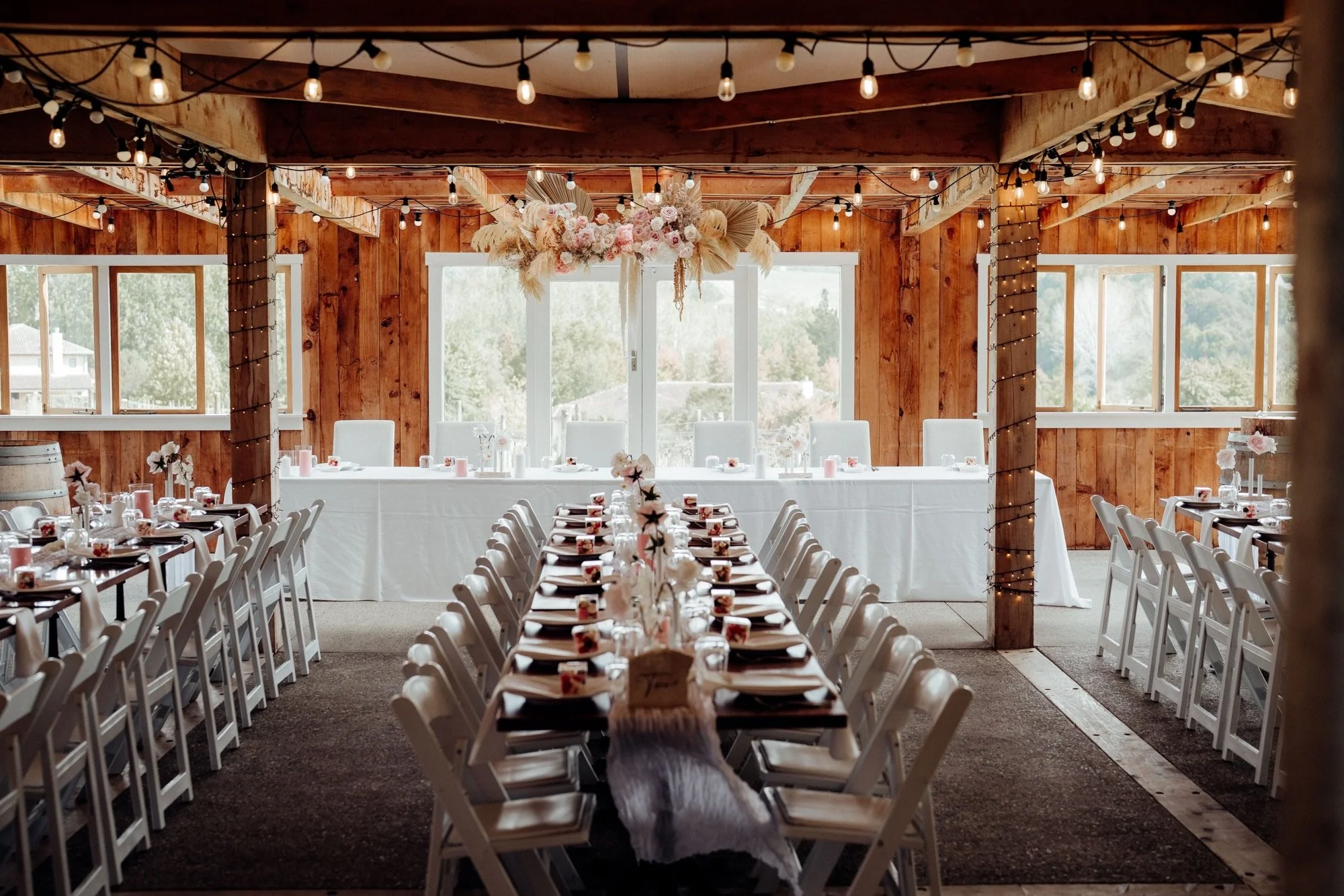 Rustic Tūranga Creek wedding reception with a suspended blush and dried floral installation above the bridal table.