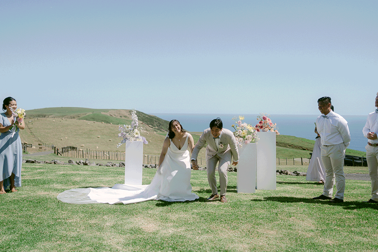 Bride and groom celebrating their ceremony between modern floral plinths overlooking the ocean at Parihoa Farm in Auckland.