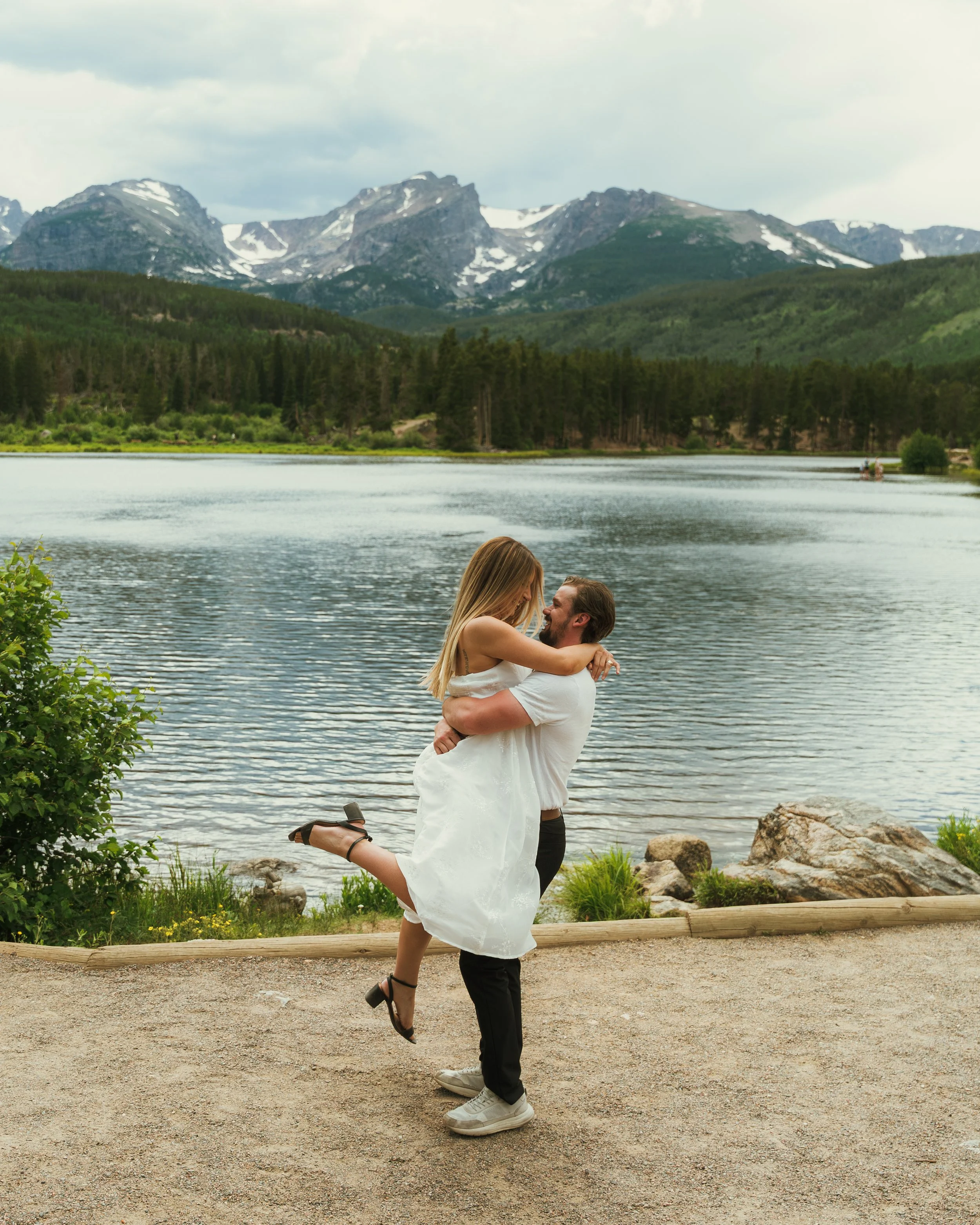 A couple dancing by a lake with mountains in the background