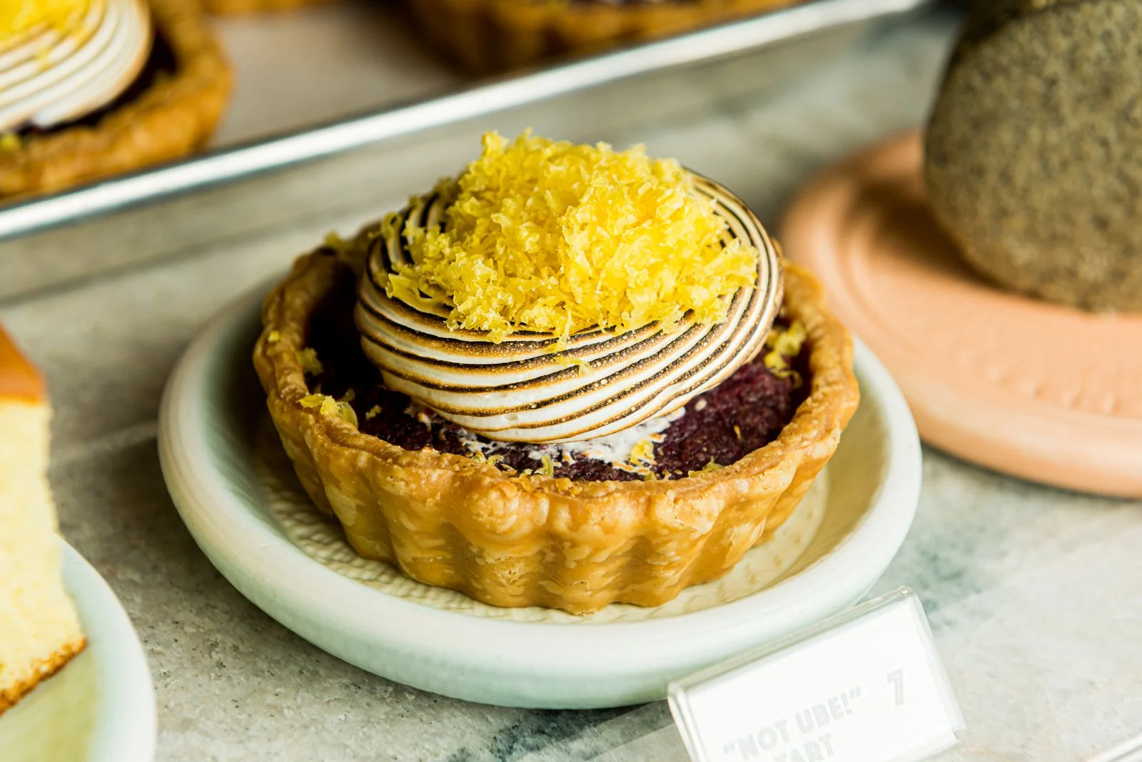 A tart filled with dark purple potato filling, topped with a spiral-shaped meringue and grated lemon zest, on a white plate.