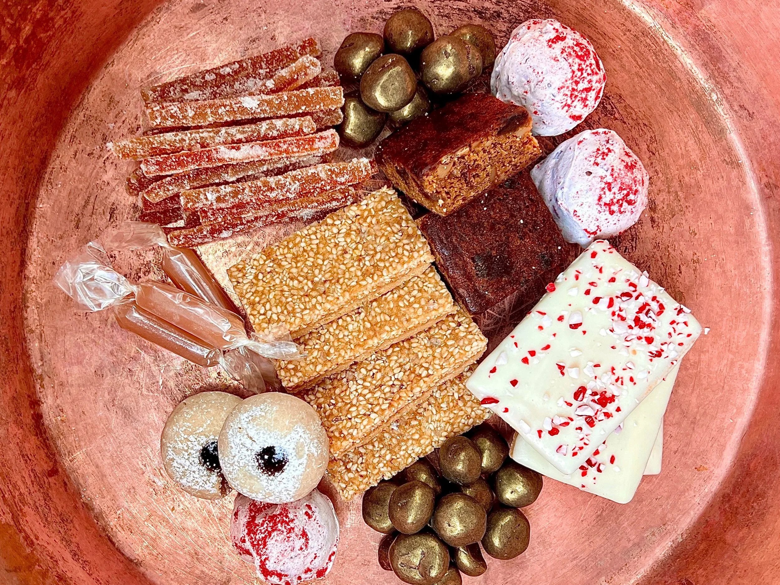Breadbelly Holiday Sweets tin 2025 featuring assorted holiday cookies and candies on a copper tray, including sugar-coated citrus slices, caramels, sesame crackers, brownies, and peppermint bark.