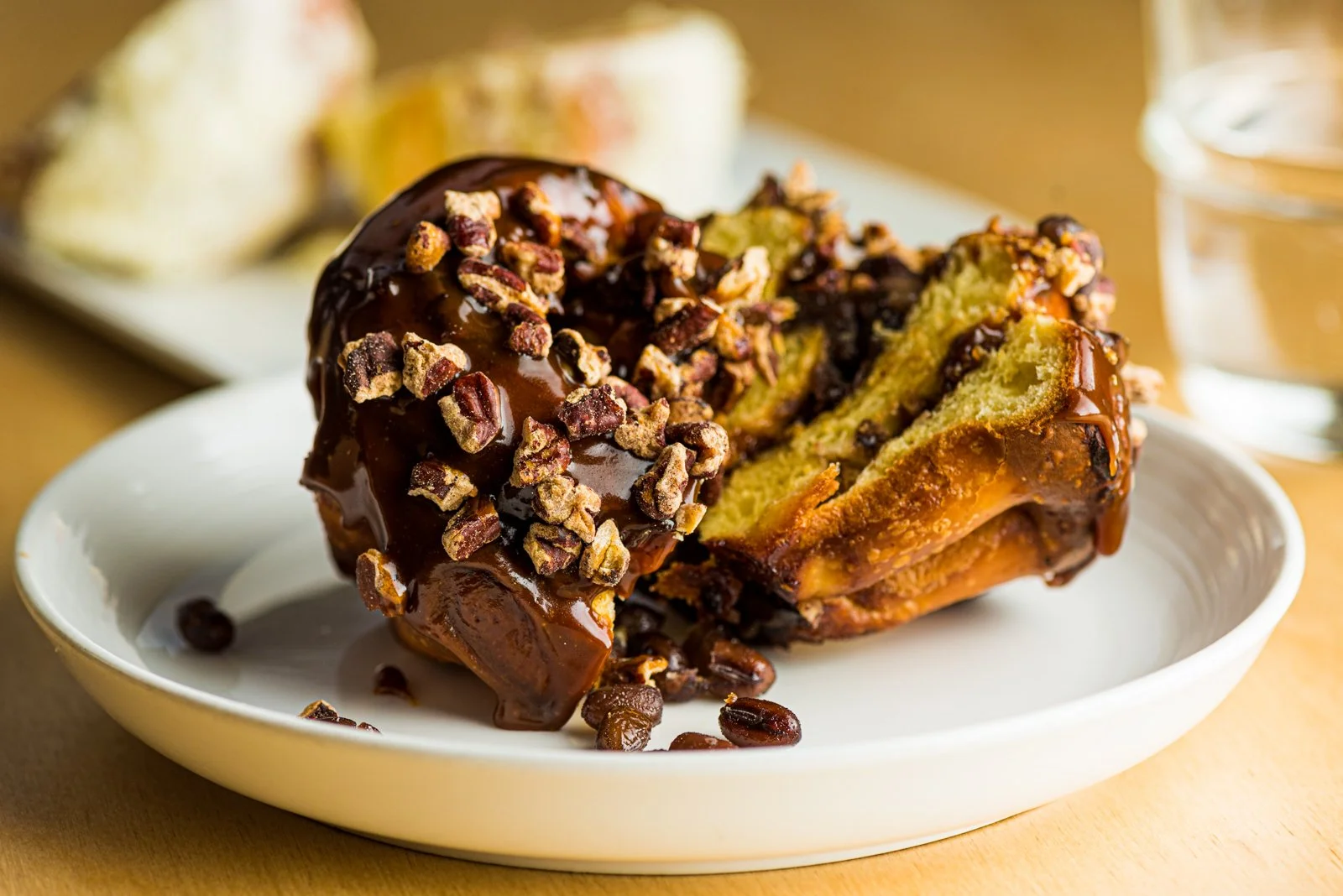 A glazed morning bun with chopped nuts on a white plate.