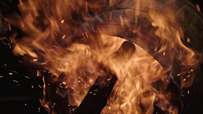 Close-up of a metal wheel on fire with flames and sparks around it.