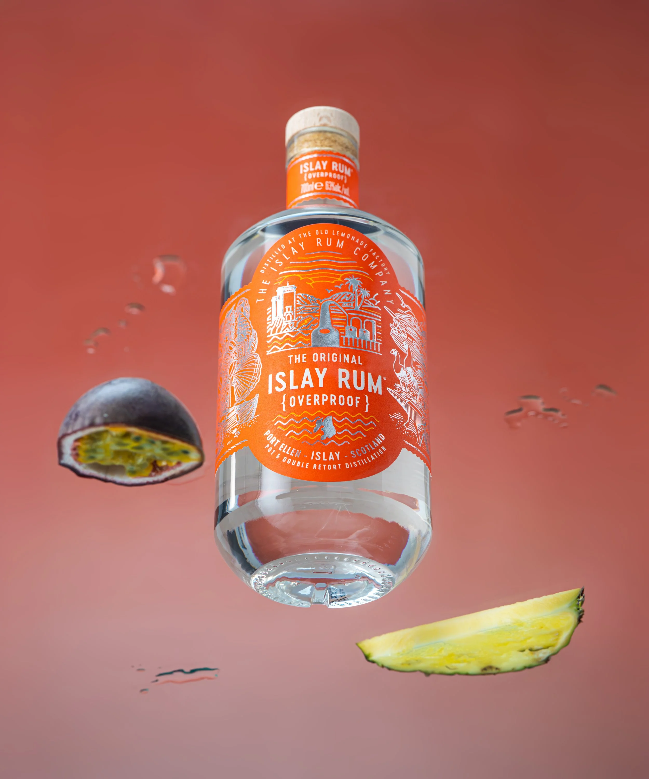 Bottle of Isla Rum with a pineapple slice and a slice of passion fruit on a pink surface.
