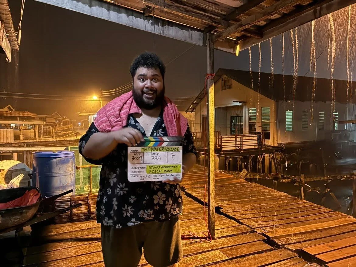 Actor LAWRENCE OLA is posing for a picture with a  film clapper  in the Water Village located in Kampong Batu Marang in Brunei while it is raining.