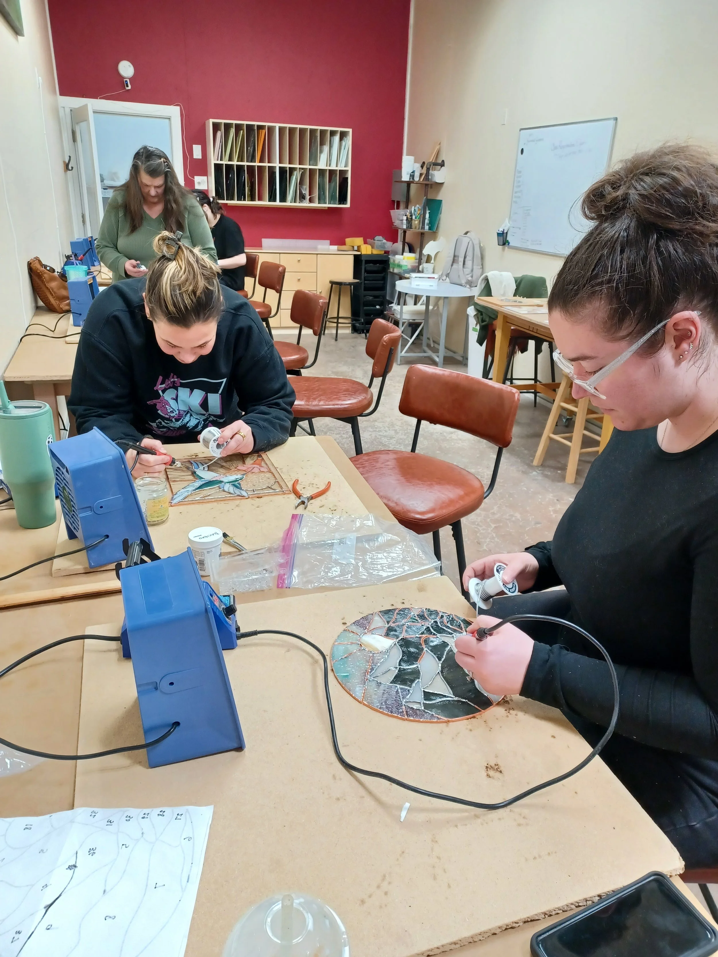 People working on stained glass art projects in a classroom setting.