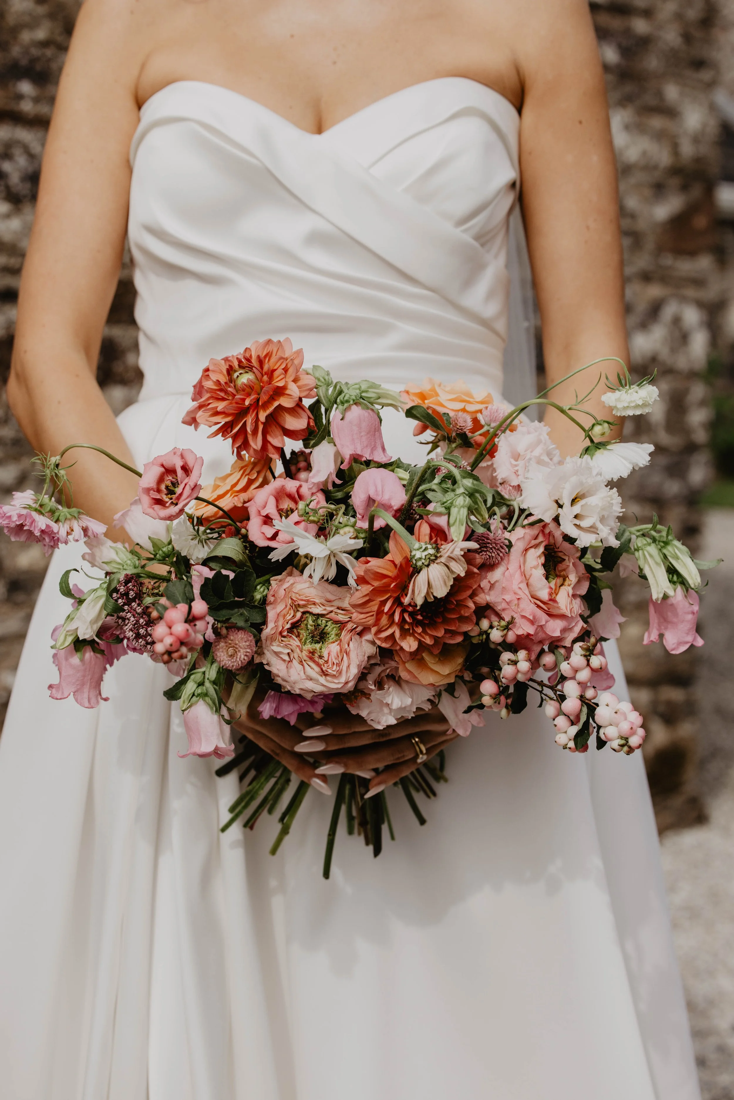 Woman in white wedding dress holding a large bouquet of pink, peach, and white flowers.