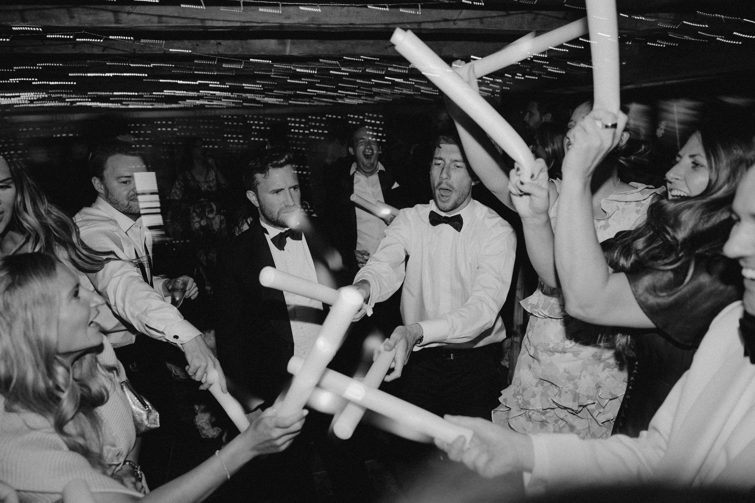 People dressed in formal attire dancing and celebrating with glow sticks in a party setting.