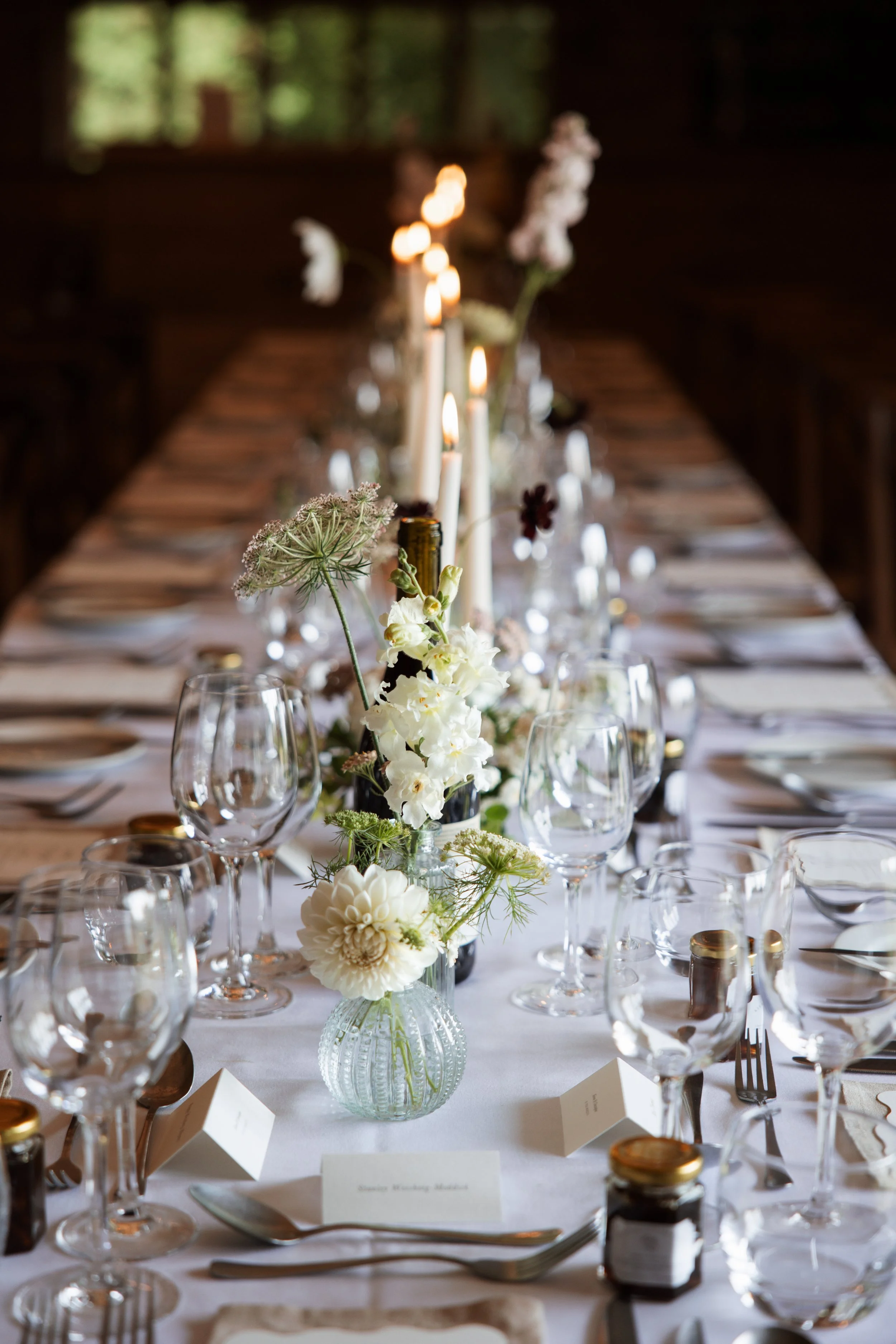 A long banquet table set for a formal event with glassware, white flowers, candles, and place cards.