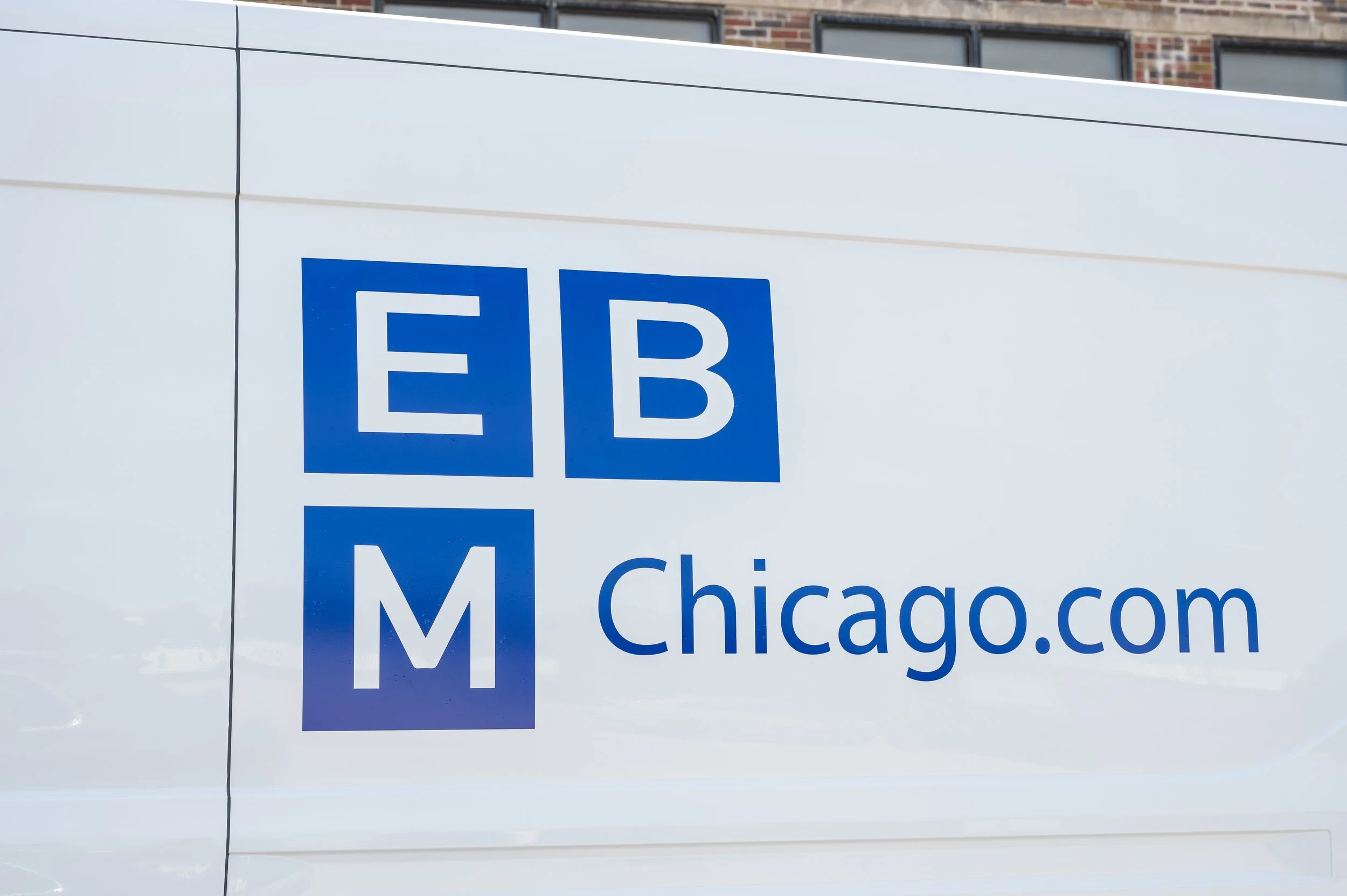 Close-up of a white vehicle with a blue logo EBMChicago.com visible on the side.